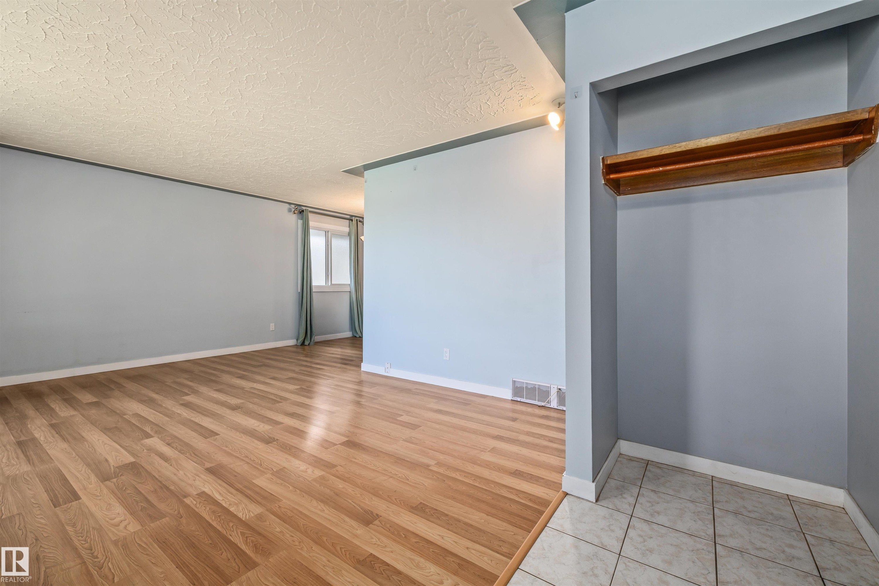 Entryway featuring a built-in wooden shelf and tile flooring, opening into a spacious room with wood-finish flooring, light blue walls, and a window with natural light - 13320 123 Street Nw, Edmonton, AB - Indoor Photo Showing Other Room