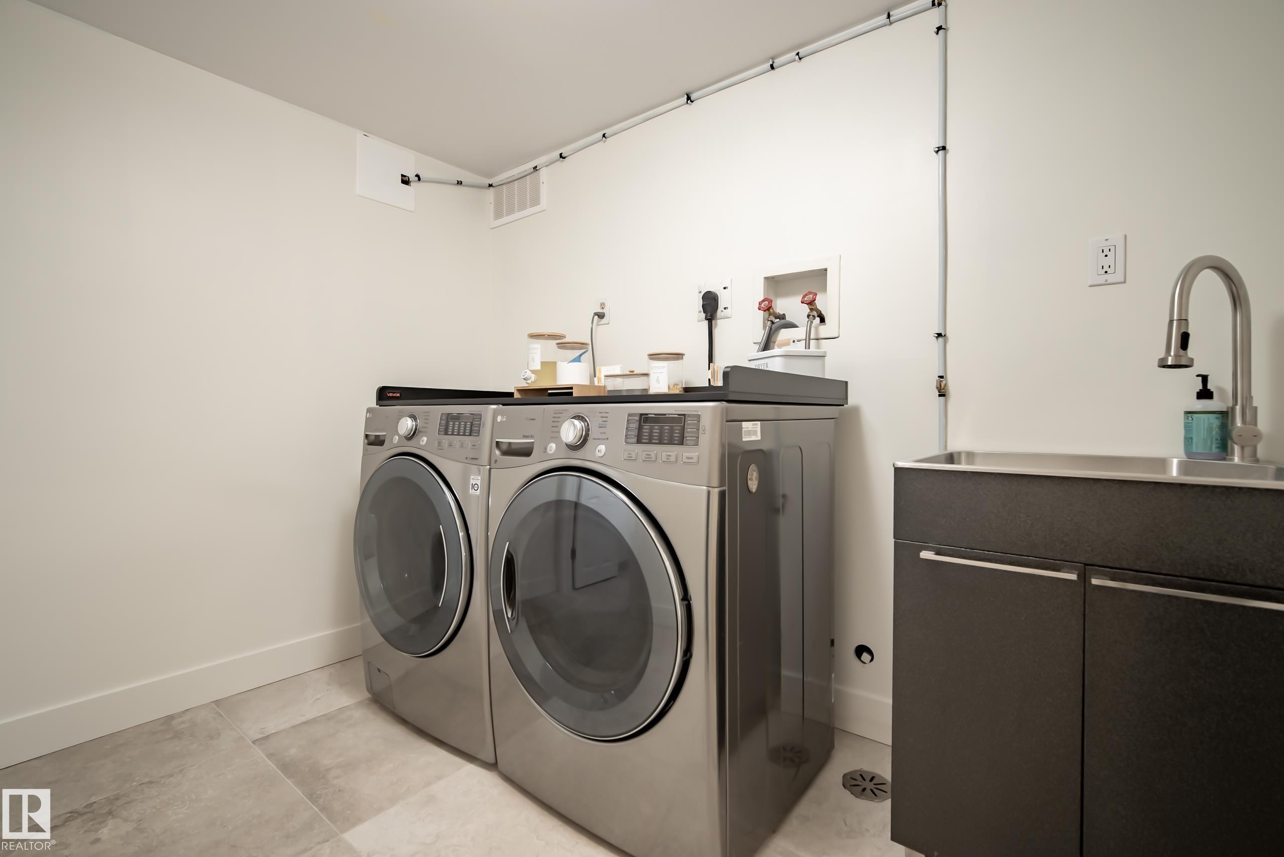 Utility room with gray tile flooring, stainless steel sink, dark cabinetry, and wall-mounted faucet - 11006 64 Avenue Nw, Edmonton, AB