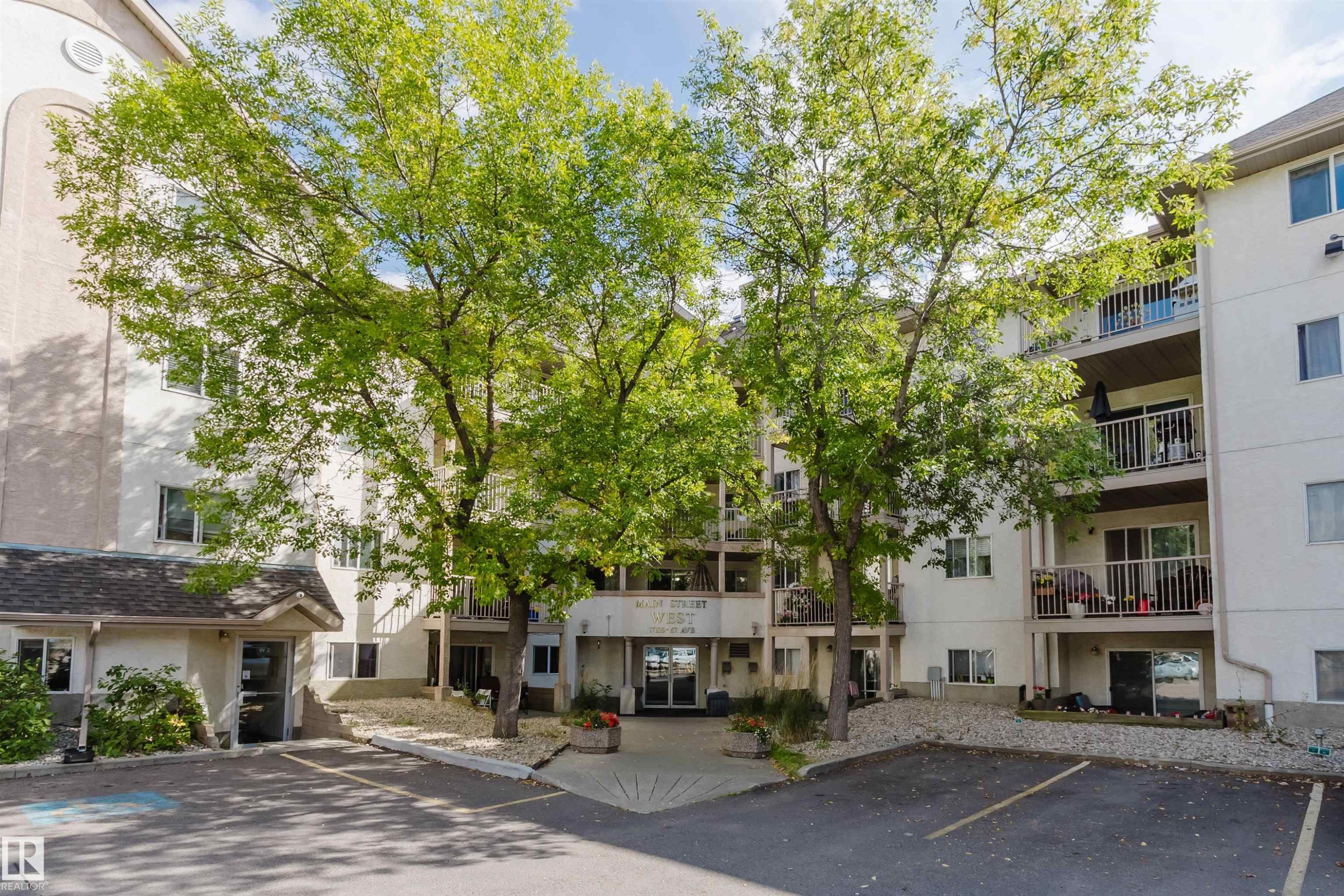 Multi-story building featuring balconies, mature trees, and a paved parking area - #316 17109 67 Av Nw, Edmonton, AB