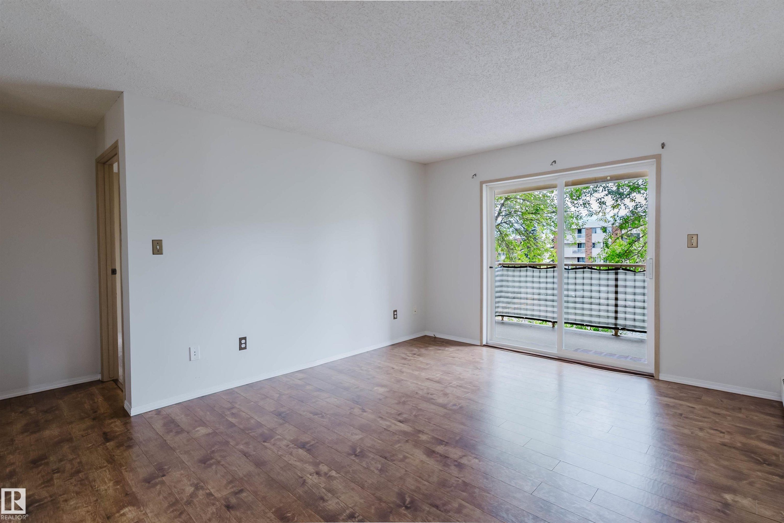 Wood-finish flooring throughout, bright white walls, and a sliding glass door leading to a balcony with metal railings - #316 17109 67 Av Nw, Edmonton, AB