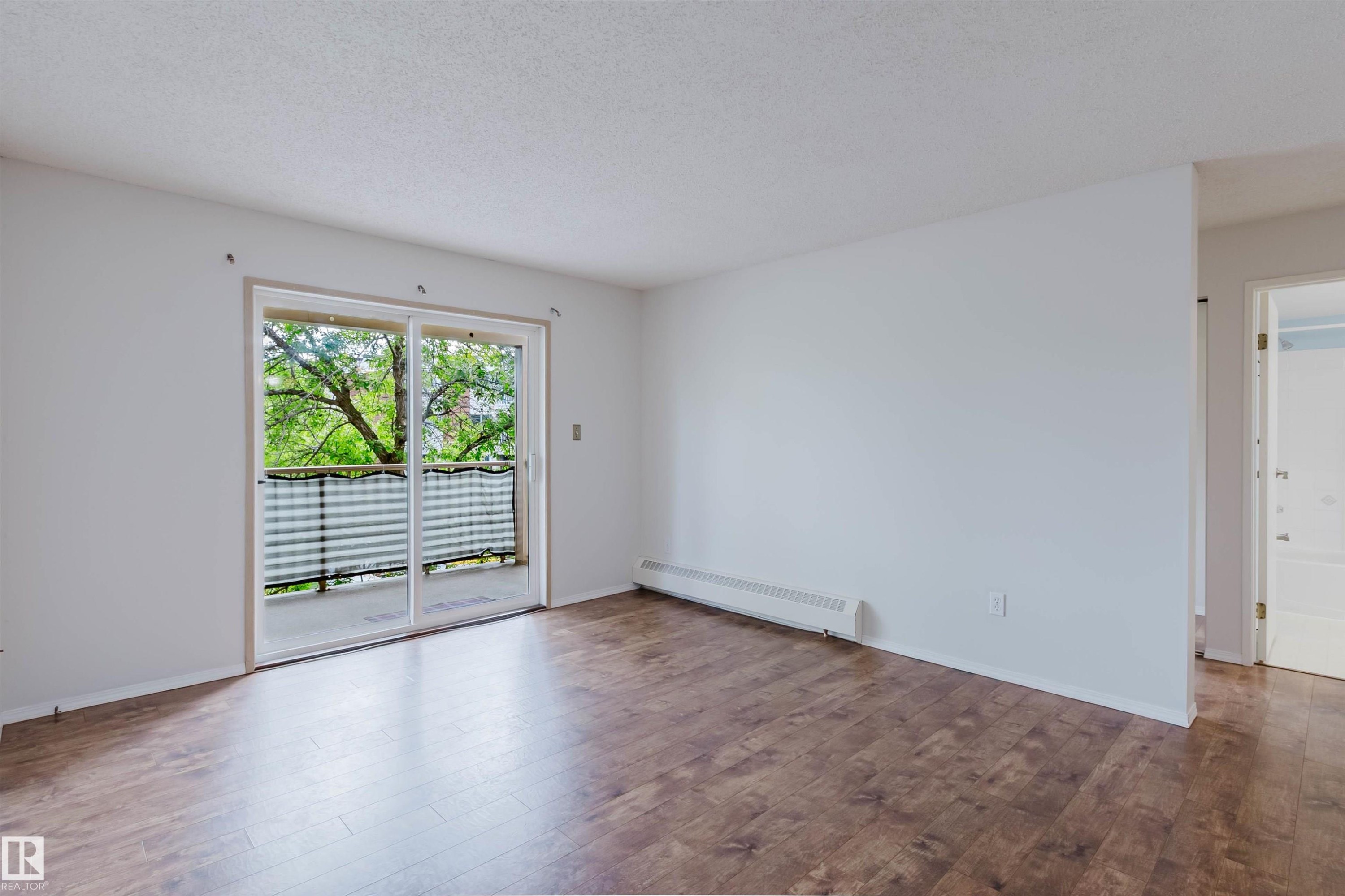 Wood-finish flooring, white walls, and sliding glass doors opening to a balcony with metal railings - #316 17109 67 Av Nw, Edmonton, AB