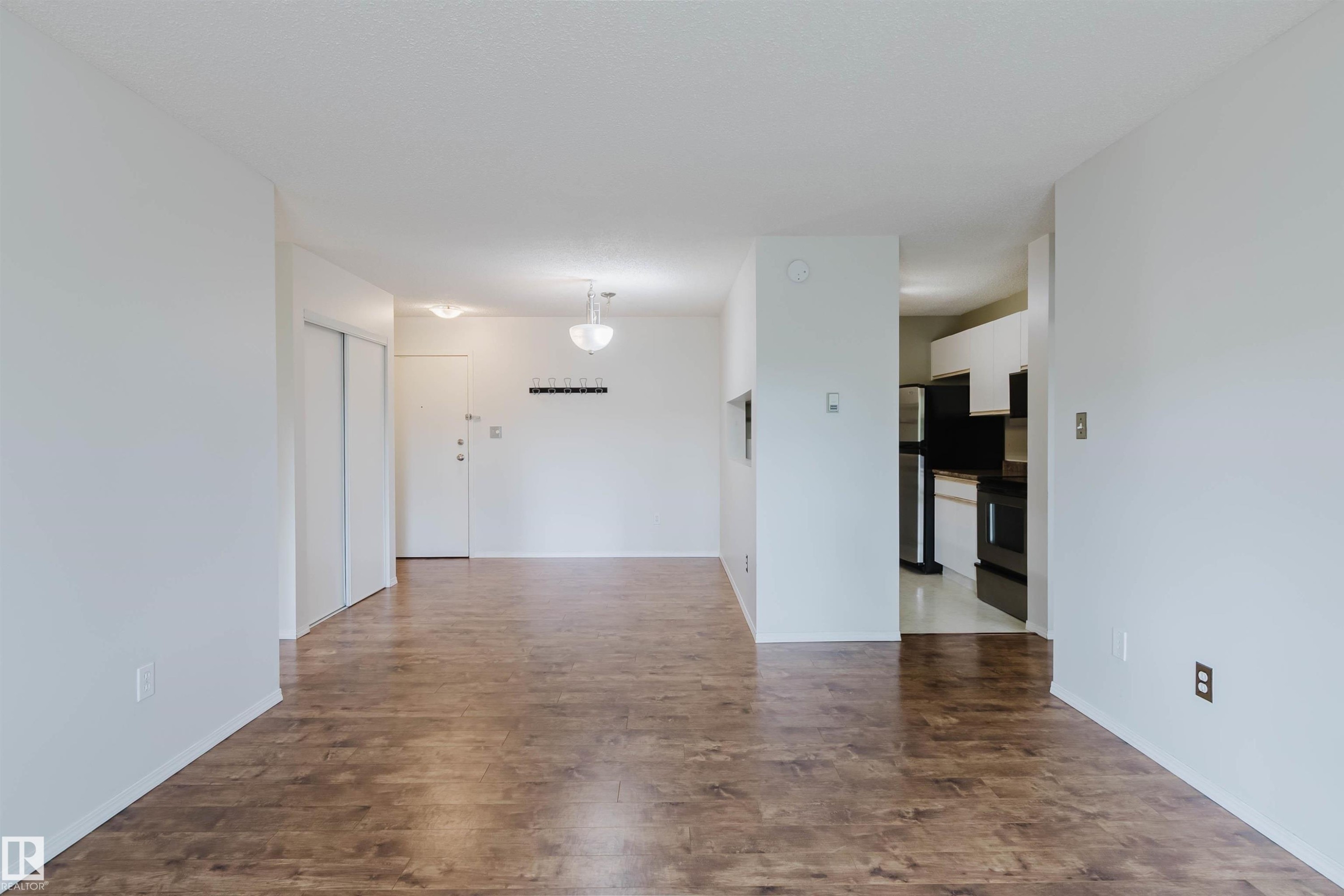 Wood-finish flooring, white walls, built-in closet with sliding doors, ceiling-mounted lighting fixtures, and an open doorway to the kitchen area - #316 17109 67 Av Nw, Edmonton, AB