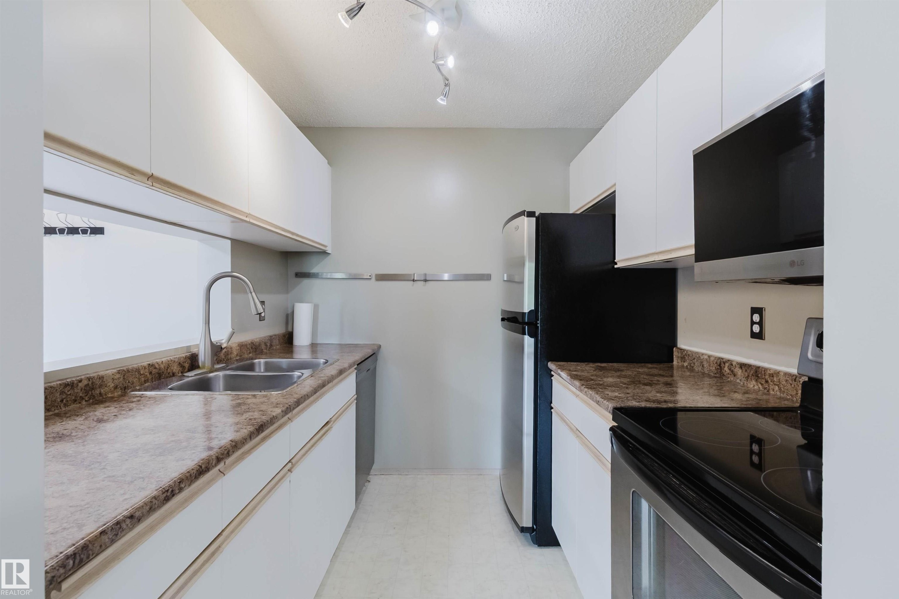 Galley kitchen featuring white cabinetry, brown patterned countertops, stainless steel appliances, a dual basin sink, and a built-in microwave - #316 17109 67 Av Nw, Edmonton, AB