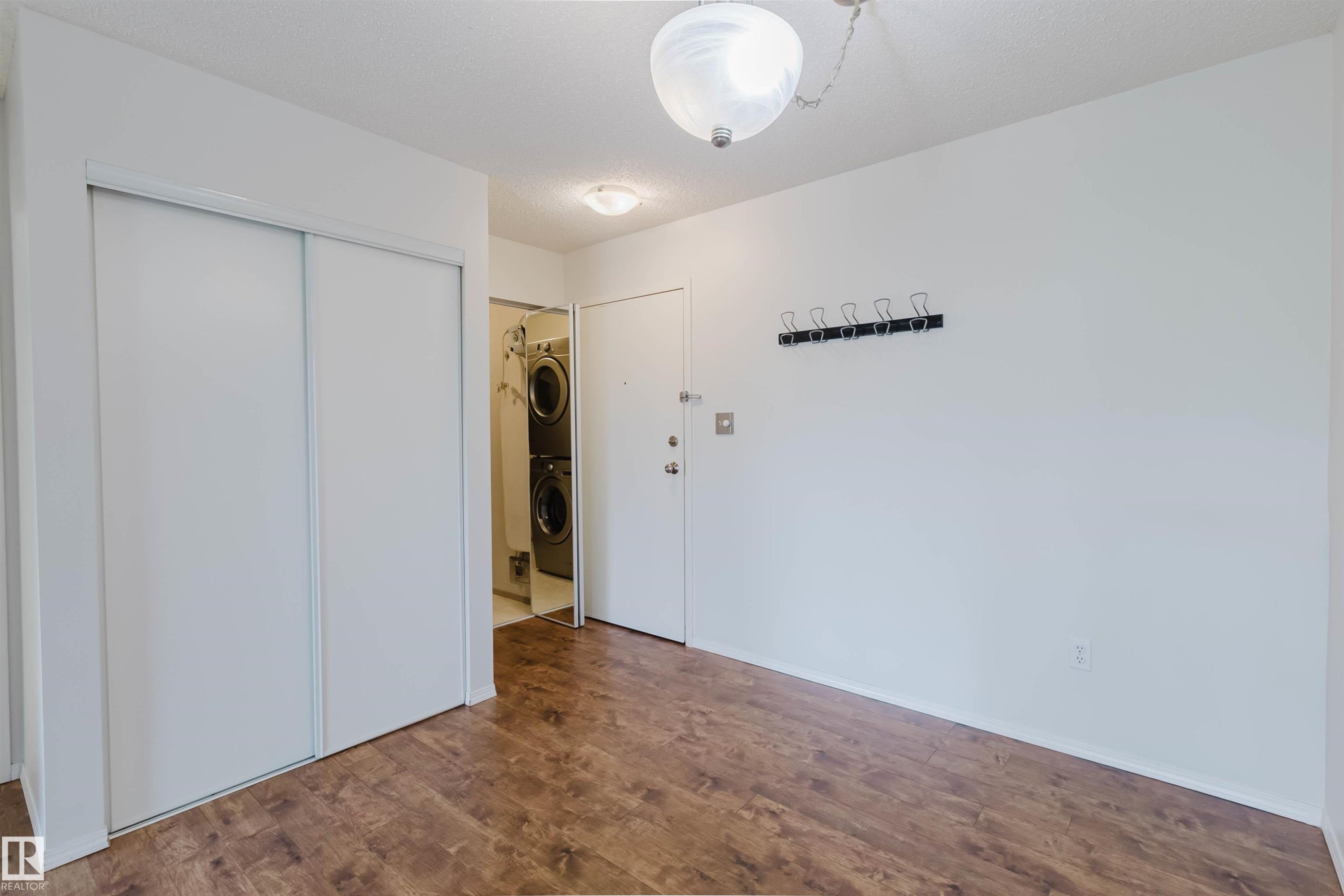 Wood-finish flooring throughout, white sliding closet doors, ceiling-mounted light fixture, and a built-in stacked washer and dryer - #316 17109 67 Av Nw, Edmonton, AB