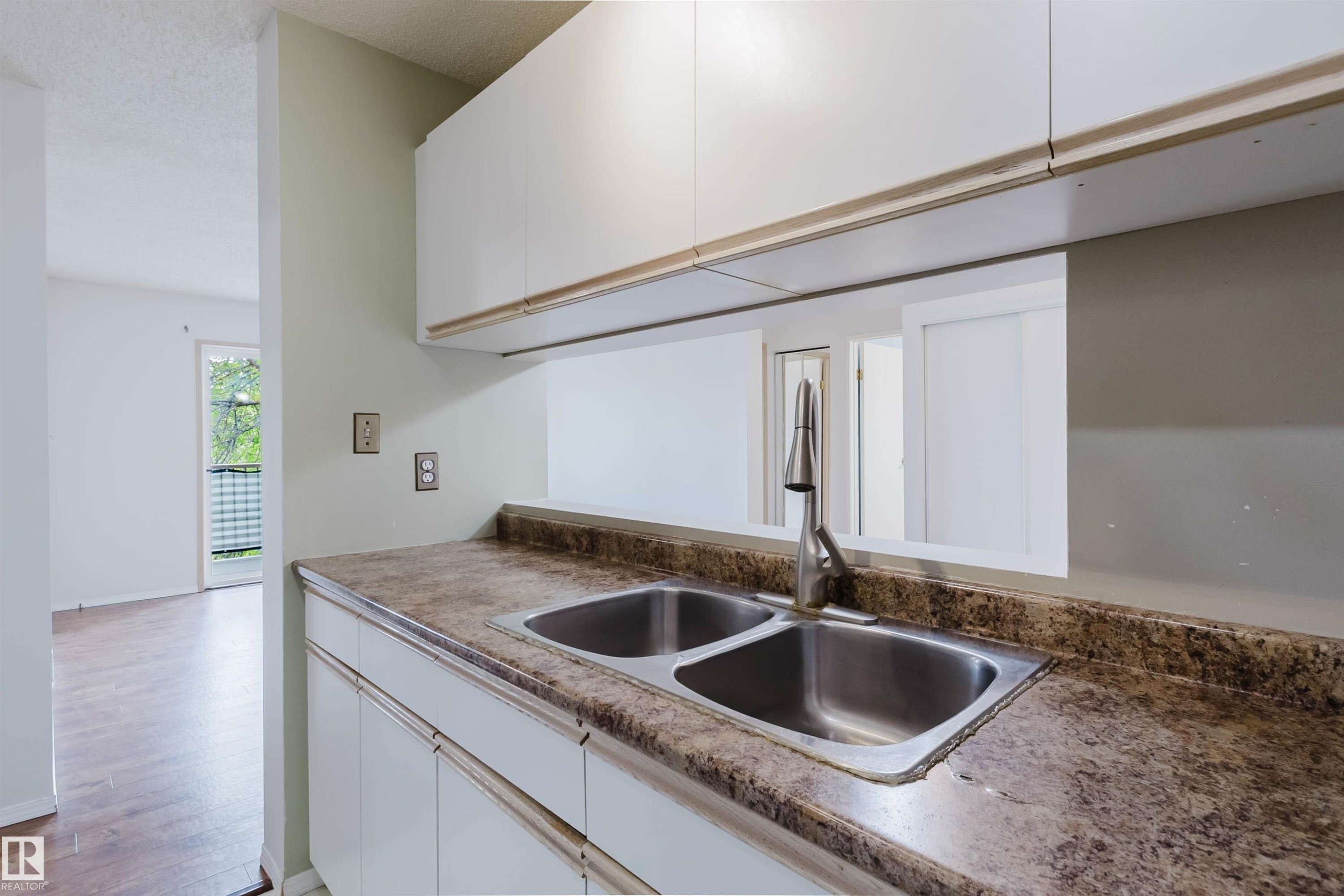 Dual basin stainless steel sink with a high-arc faucet, solid surface countertop, white cabinetry, and wood-finish flooring - #316 17109 67 Av Nw, Edmonton, AB