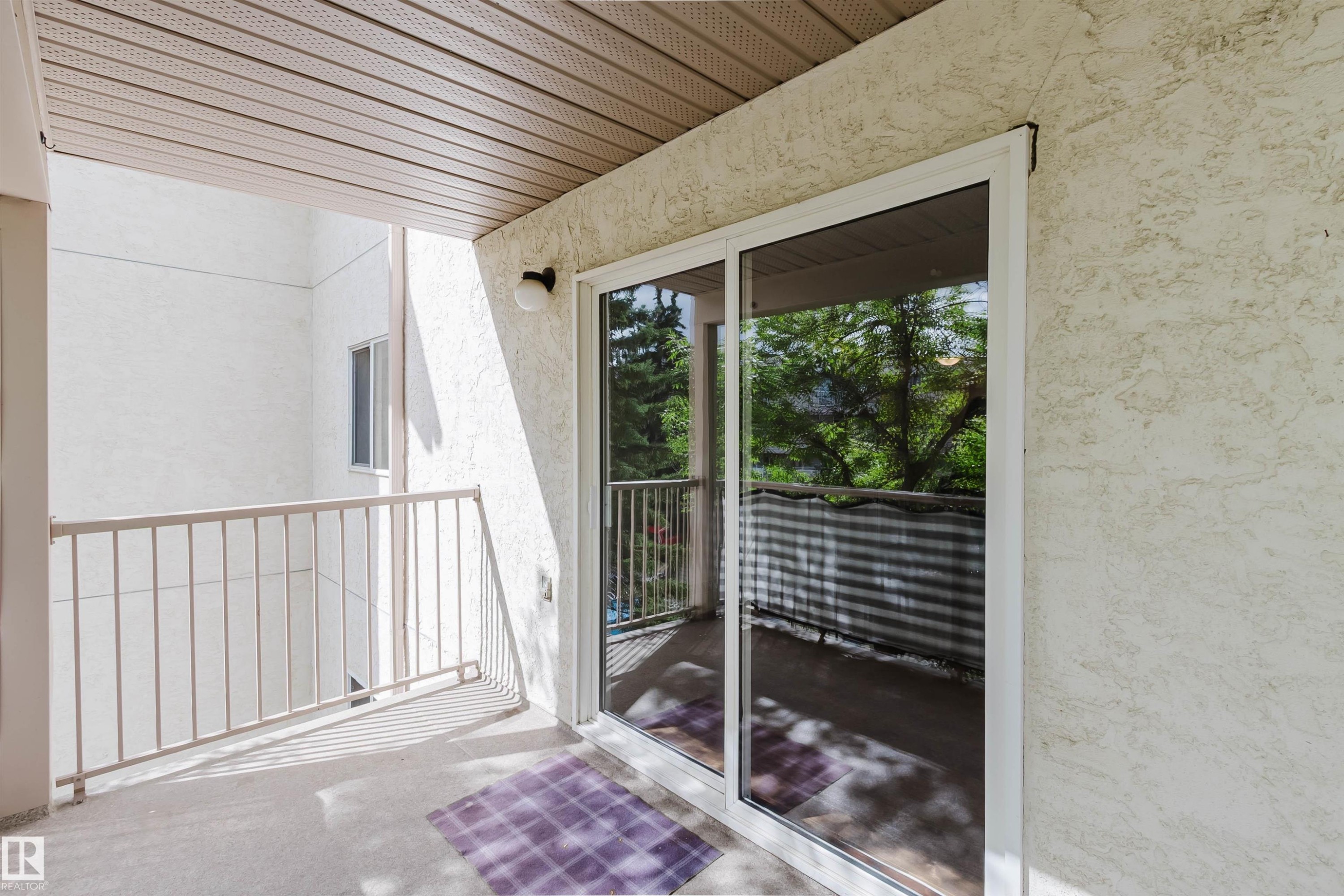 Balcony with a textured stucco exterior, white metal railing, and a sliding glass door - #316 17109 67 Av Nw, Edmonton, AB