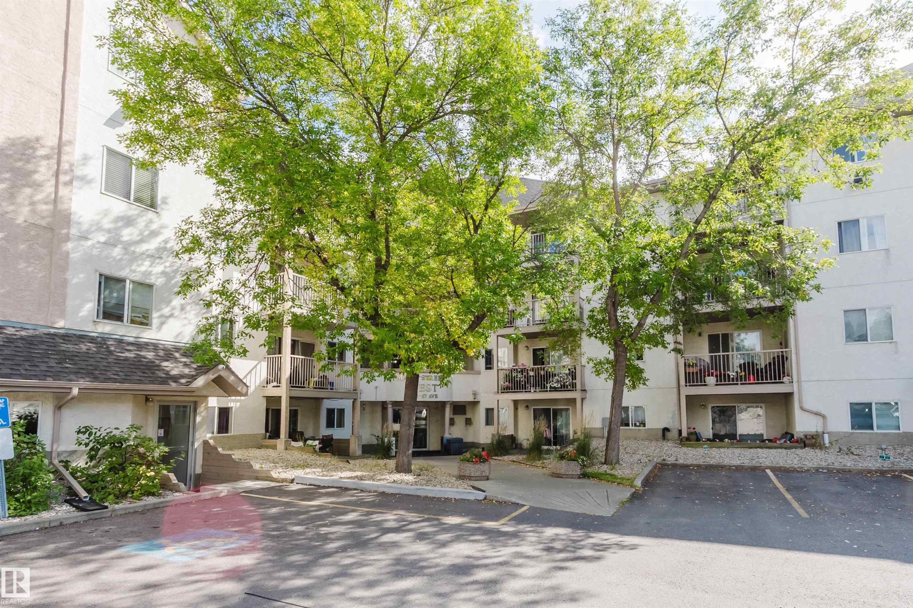 Multi-story building exterior with individual balconies, paved parking, established trees, and a covered entry - #316 17109 67 Av Nw, Edmonton, AB