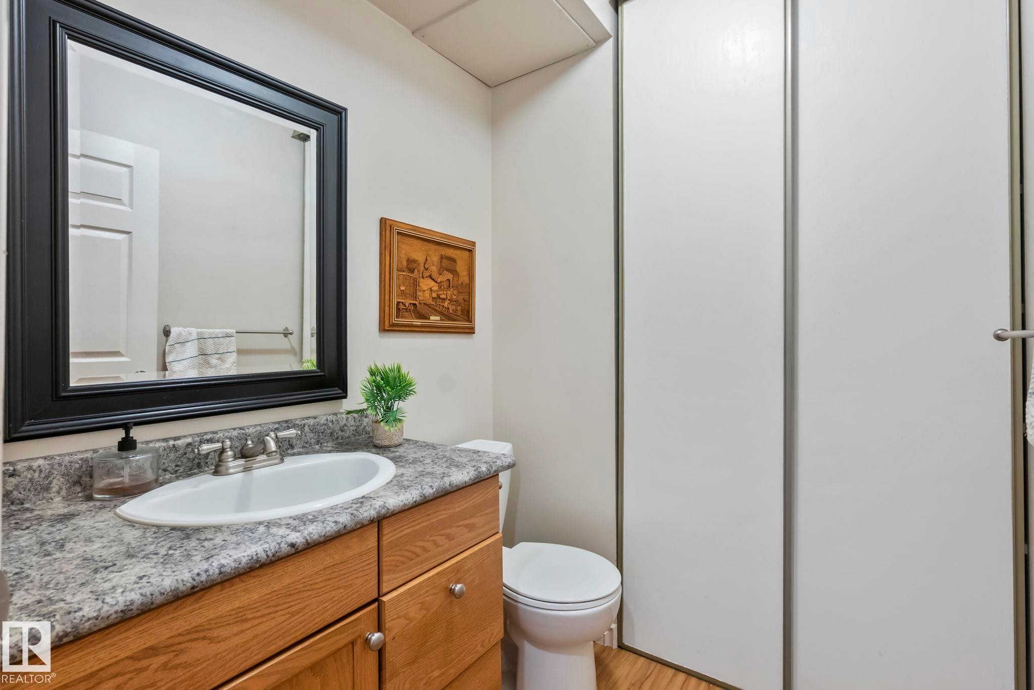 Vanity with an integrated sink, wood-finish cabinetry, a framed mirror, and a toilet - 716 Clareview Rd Nw, Edmonton, AB