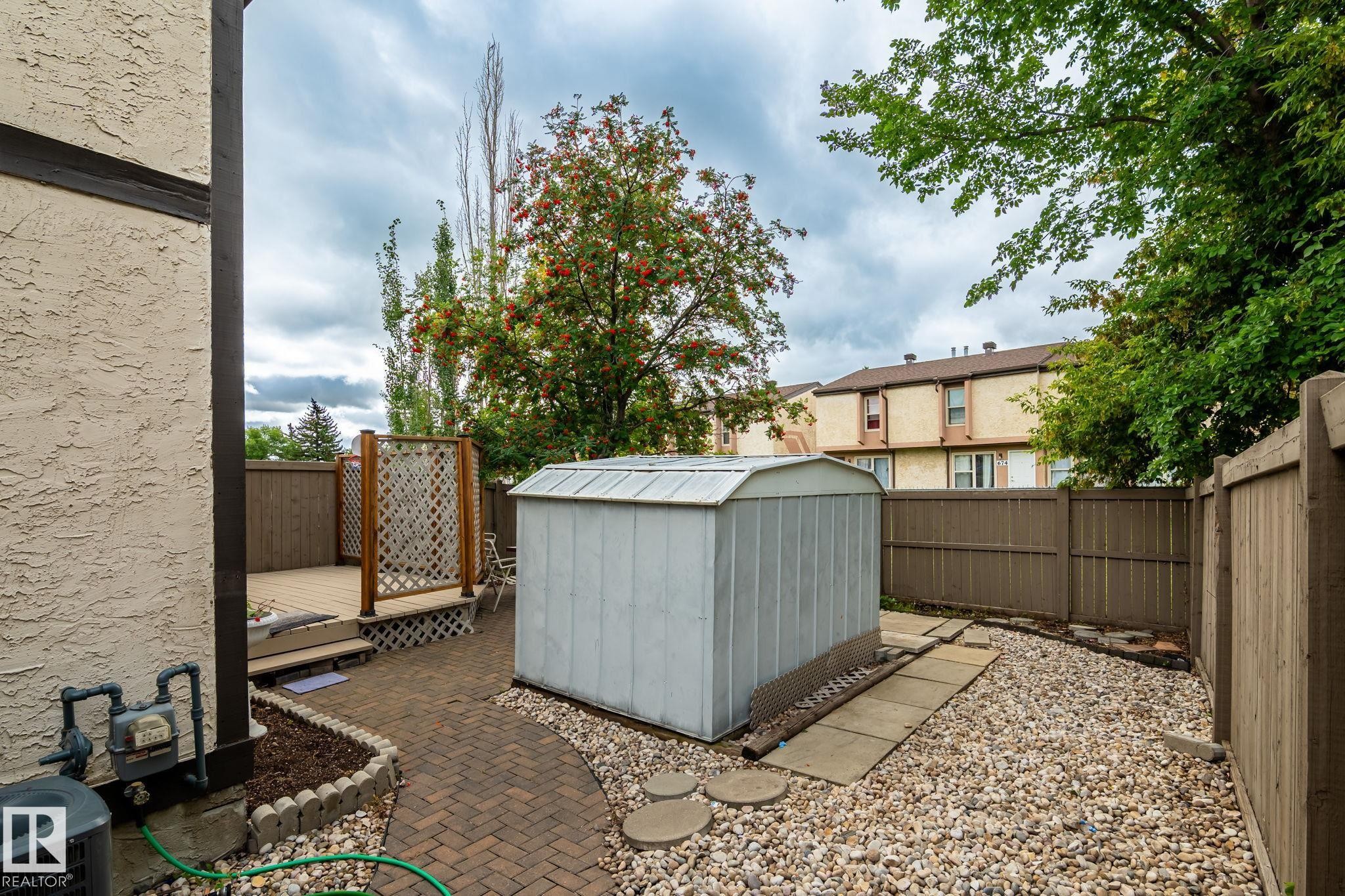 Outdoor space featuring a raised wood deck with lattice detailing, a brick paver pathway, a gravel ground covering, and a storage shed - 716 Clareview Rd Nw, Edmonton, AB