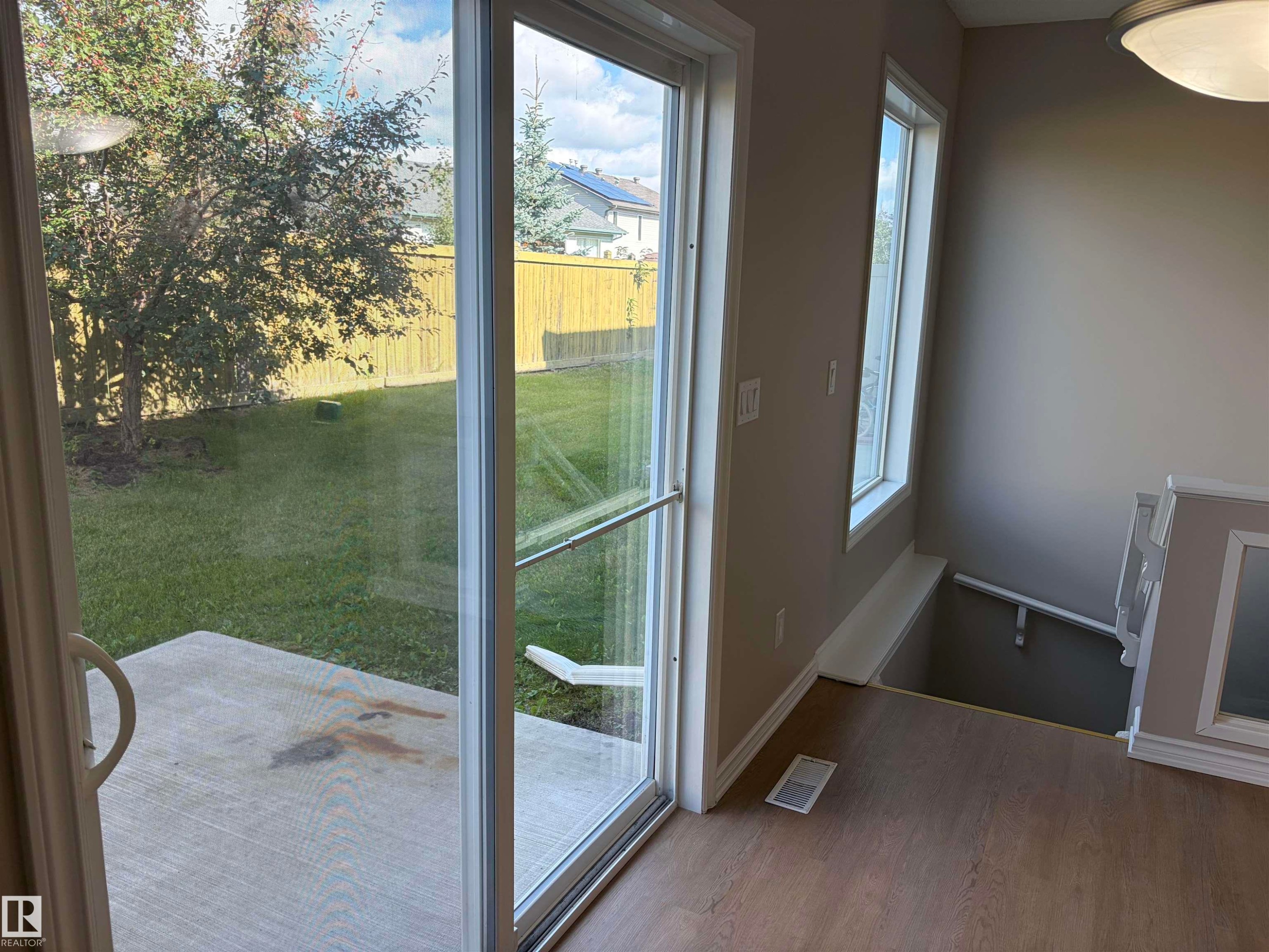 Sliding glass door opening to a concrete patio and green lawn - #100 13825 155 Av Nw, Edmonton, AB