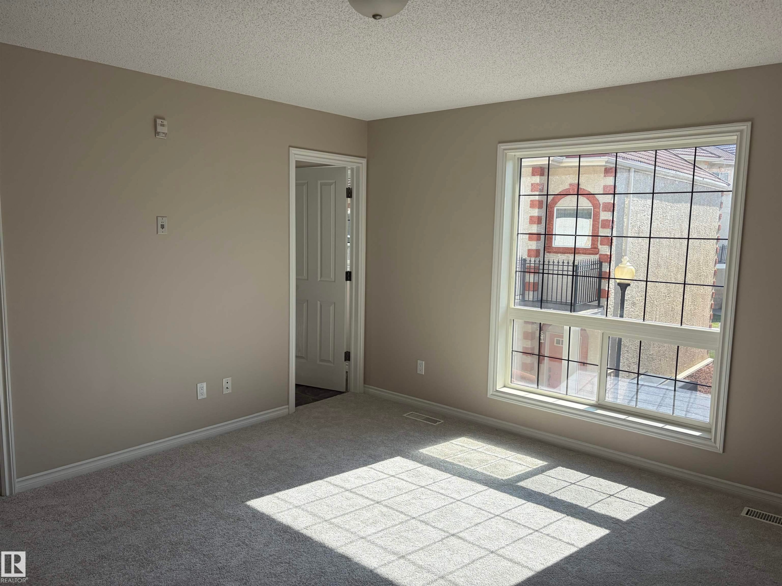 Neutral tone wall paint, light gray carpeting, white trim, and a window with grid inserts - #100 13825 155 Av Nw, Edmonton, AB