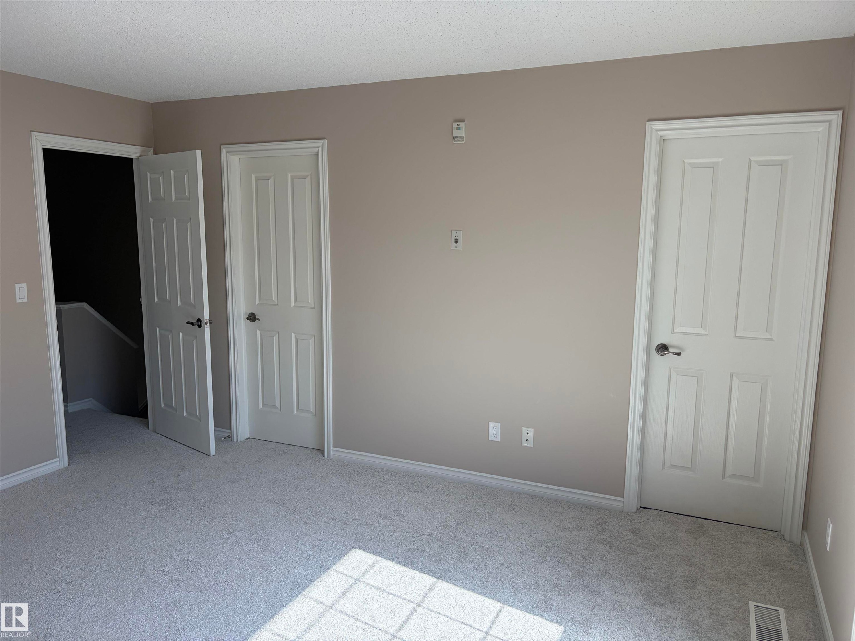 Neutral wall paint, white trim, light-colored carpeting, and three paneled doors - #100 13825 155 Av Nw, Edmonton, AB