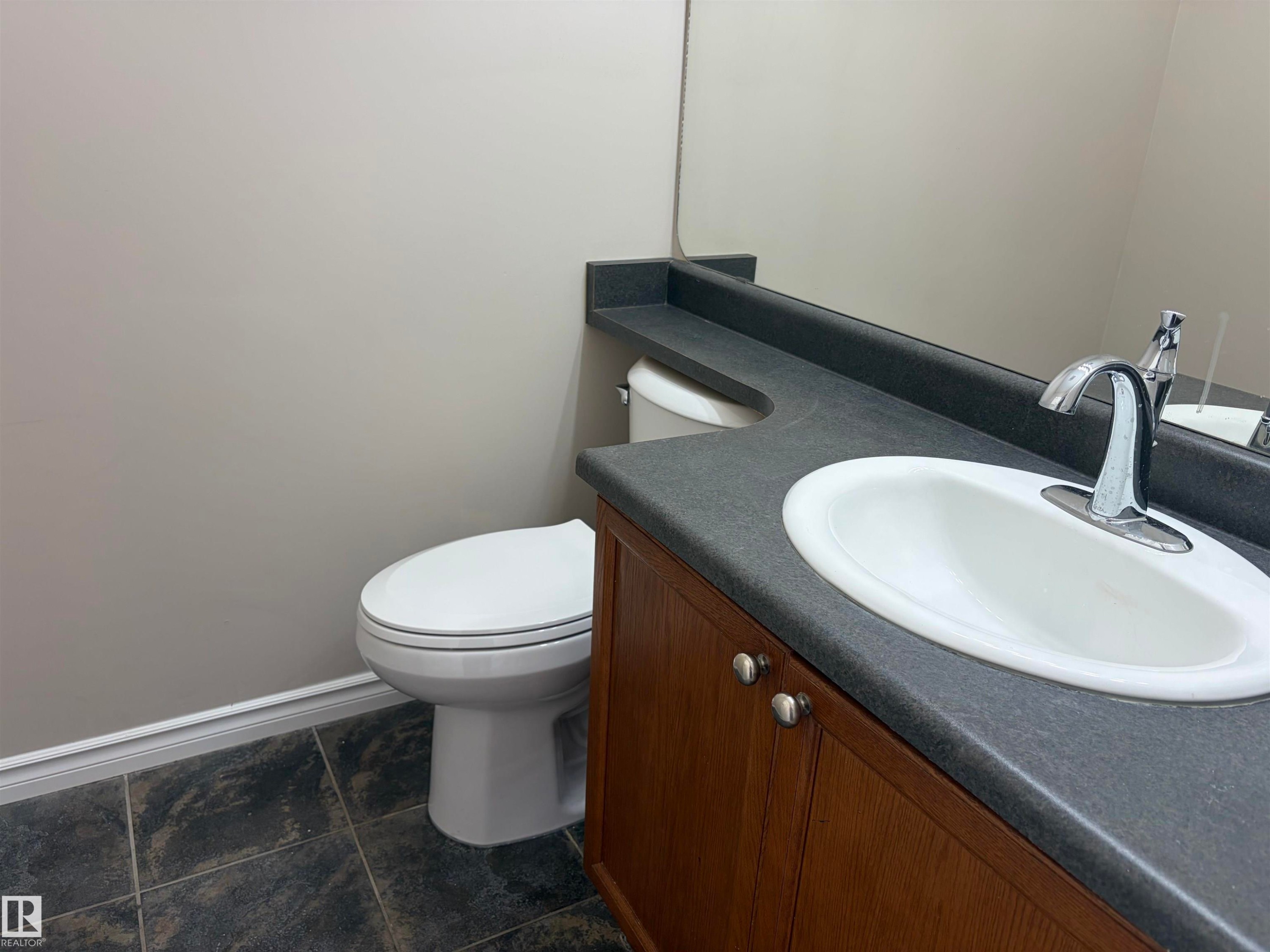 Wood-finish vanity with dual cabinet doors, integrated sink, chrome faucet, and a dark countertop - #100 13825 155 Av Nw, Edmonton, AB