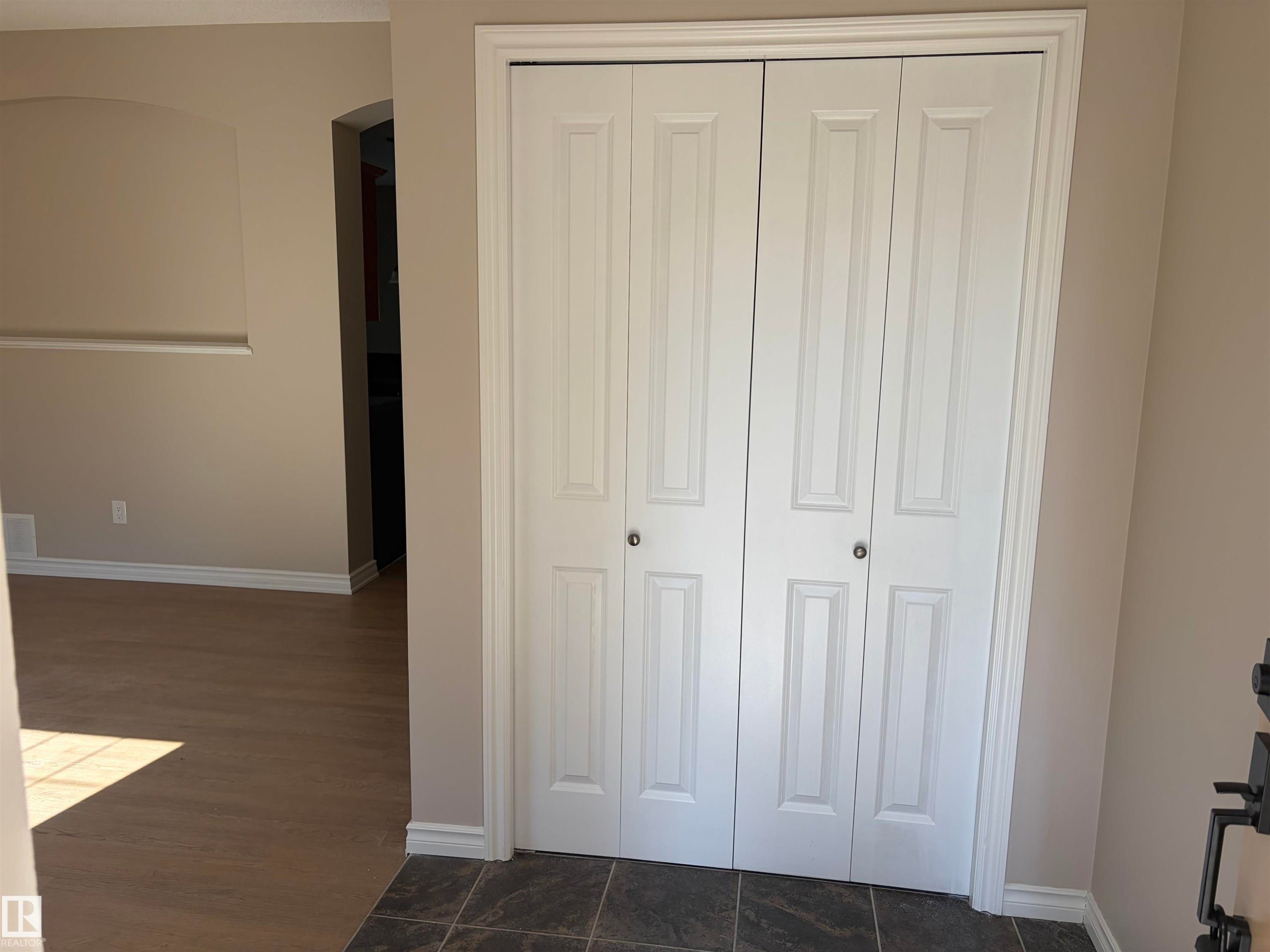 White bi-fold closet doors, tile flooring, wood-finish flooring, light neutral wall paint, and white trim - #100 13825 155 Av Nw, Edmonton, AB