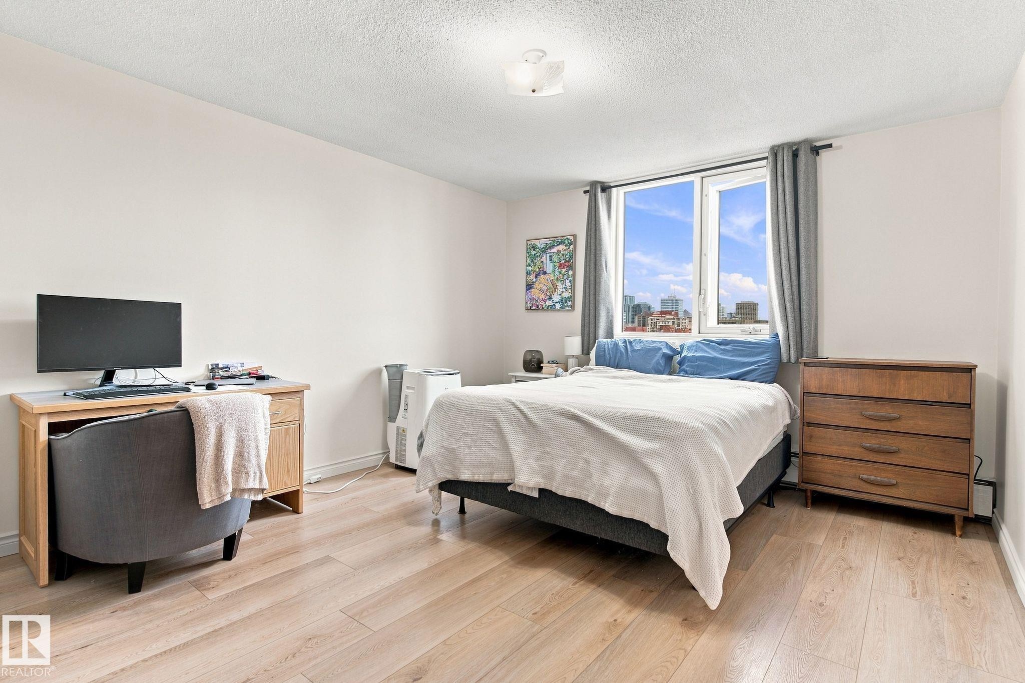 Light wood-finish flooring, white walls, and a large window with city scenery - #1507 9835 113 St Nw, Edmonton, AB