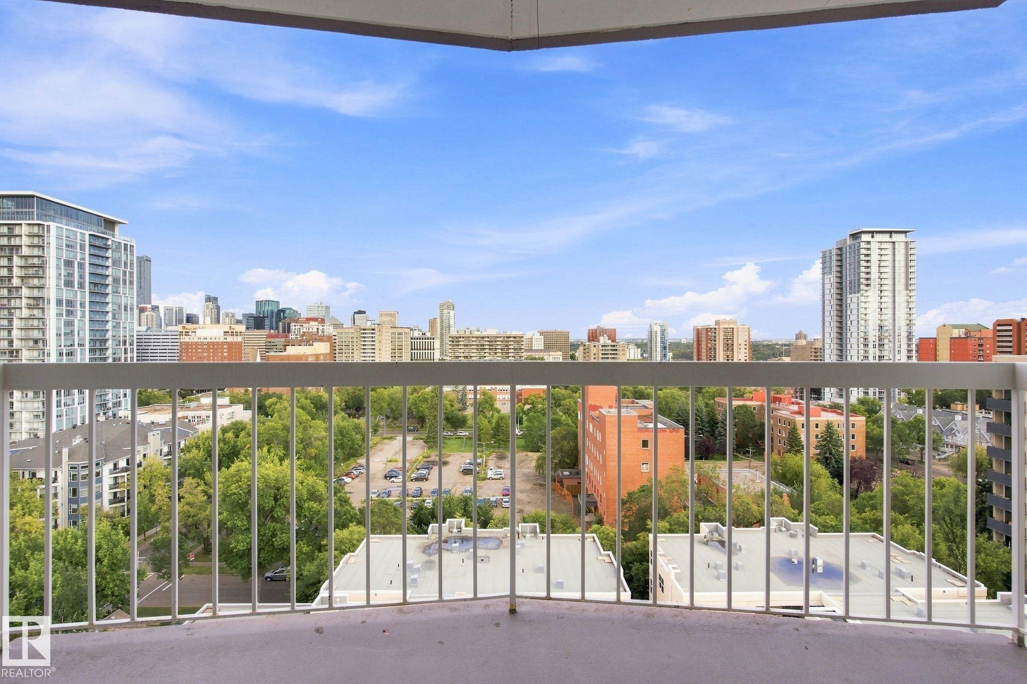 Balcony with painted concrete flooring and white metal railings overlooking a city skyline, urban trees, and buildings - #1507 9835 113 St Nw, Edmonton, AB