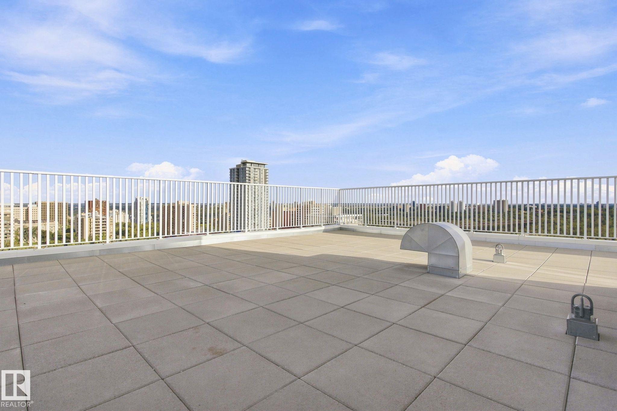Expansive rooftop terrace with light-toned rectangular paving stones and a white metal railing - #1507 9835 113 St Nw, Edmonton, AB