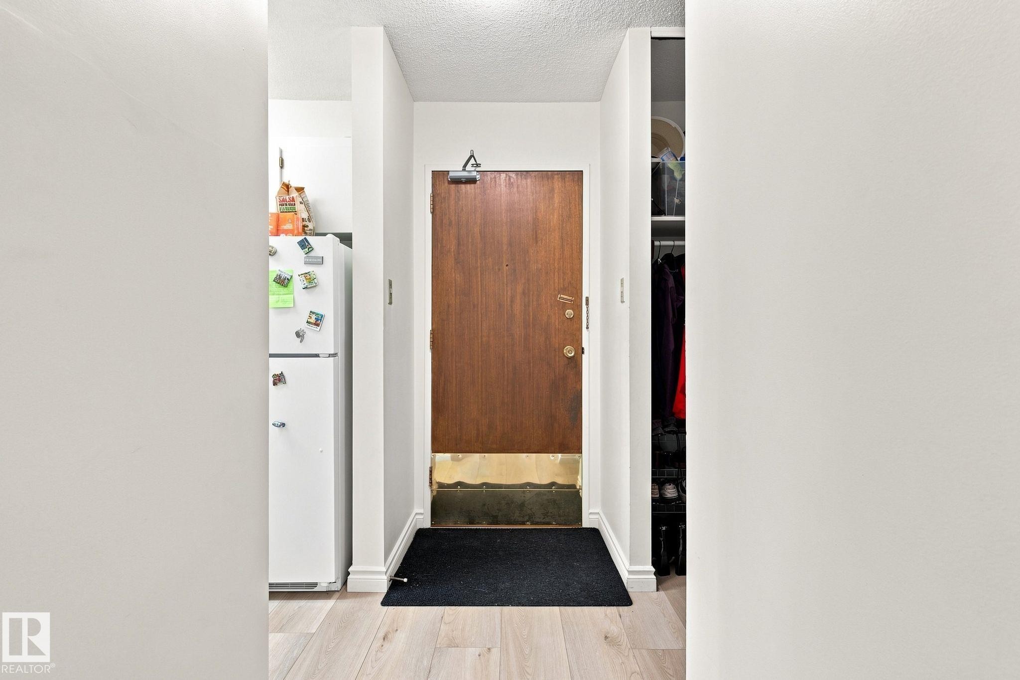 Entryway featuring wood-finish flooring, a solid wood door, and an integrated storage closet - #1507 9835 113 St Nw, Edmonton, AB