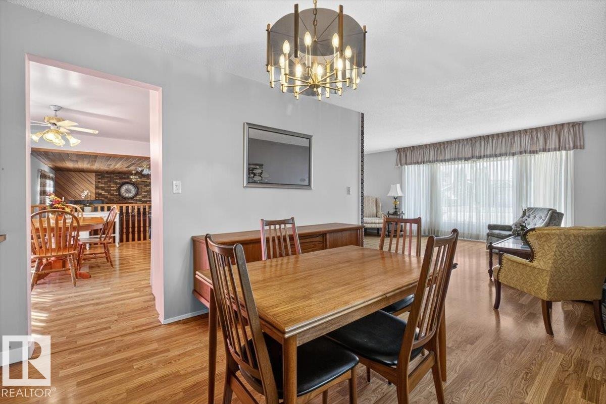 Open dining area featuring wood-finish flooring, a contemporary chandelier, light gray painted walls, and a large cased opening - 4027 74 Street Nw, Edmonton, AB - Indoor Photo Showing Dining Room