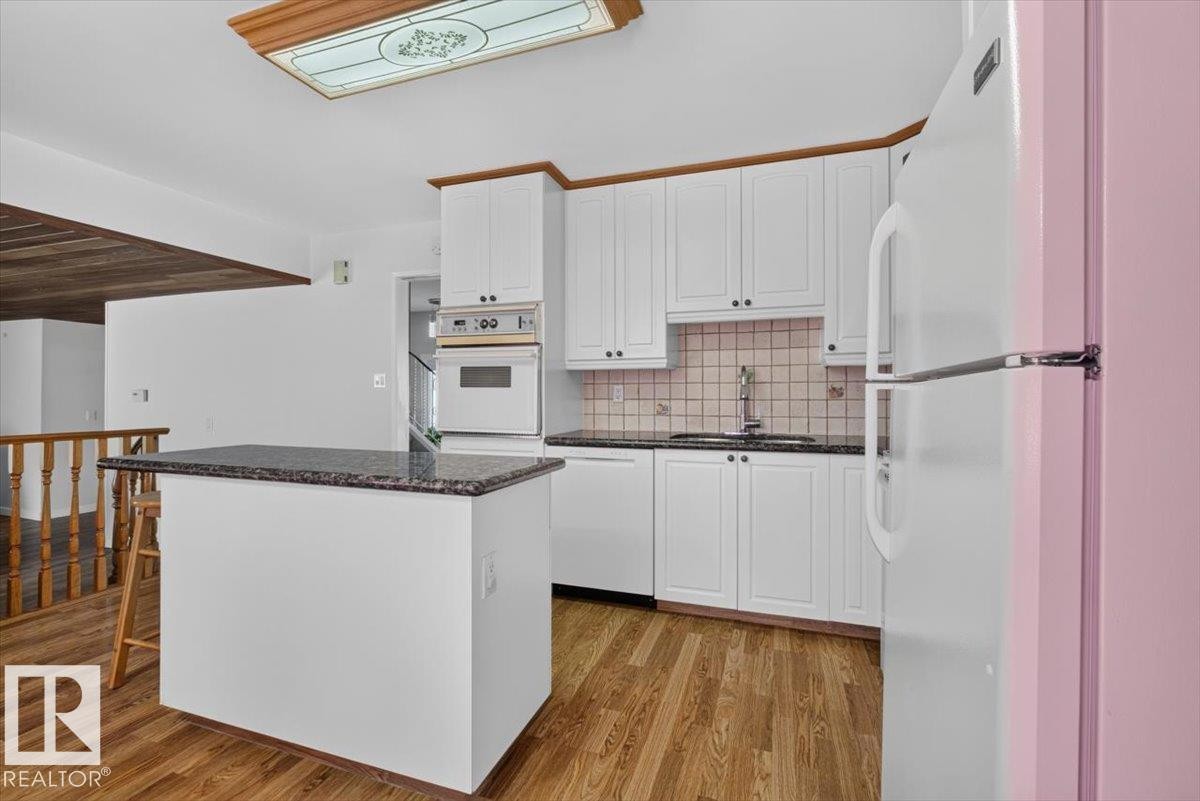 Kitchen featuring wood-finish flooring, white cabinetry, dark countertops, a built-in oven, and a central island with a contrasting dark countertop - 4027 74 Street Nw, Edmonton, AB - Indoor Photo Showing Kitchen