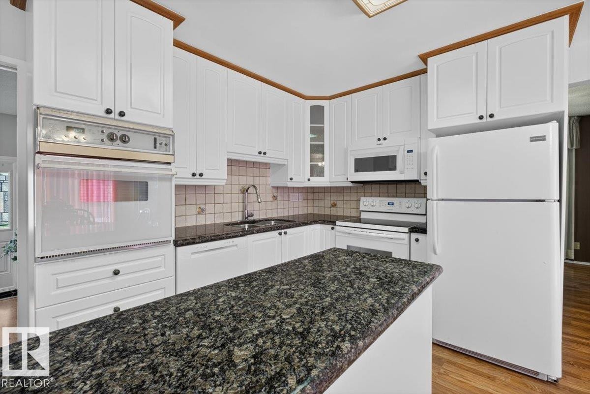 Kitchen featuring white cabinetry with dark hardware, dark patterned countertops, integrated wall oven, and white appliances - 4027 74 Street Nw, Edmonton, AB - Indoor Photo Showing Kitchen