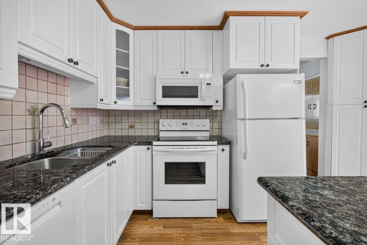 Kitchen featuring white cabinetry, dark speckled countertops, and wood-finish flooring - 4027 74 Street Nw, Edmonton, AB - Indoor Photo Showing Kitchen With Double Sink