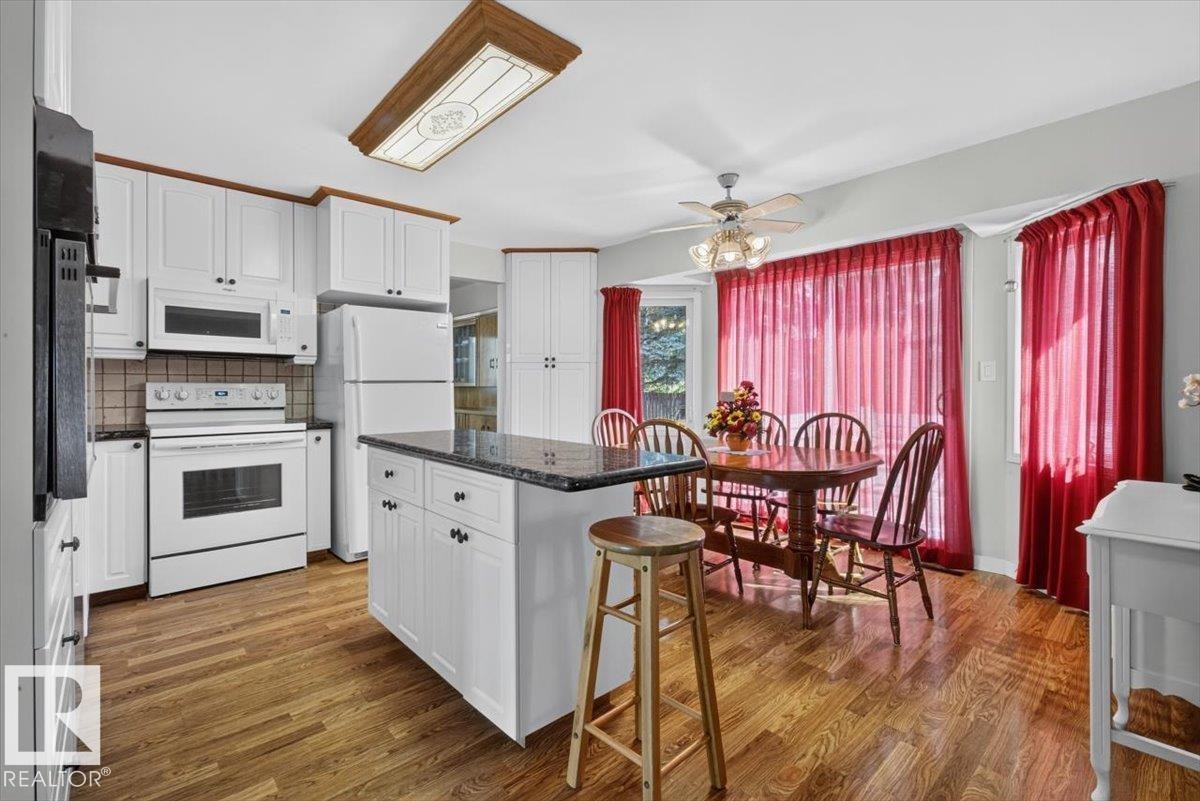 Kitchen featuring white cabinetry, dark countertops, wood-finish flooring, white appliances, and a central island - 4027 74 Street Nw, Edmonton, AB - Indoor Photo Showing Kitchen