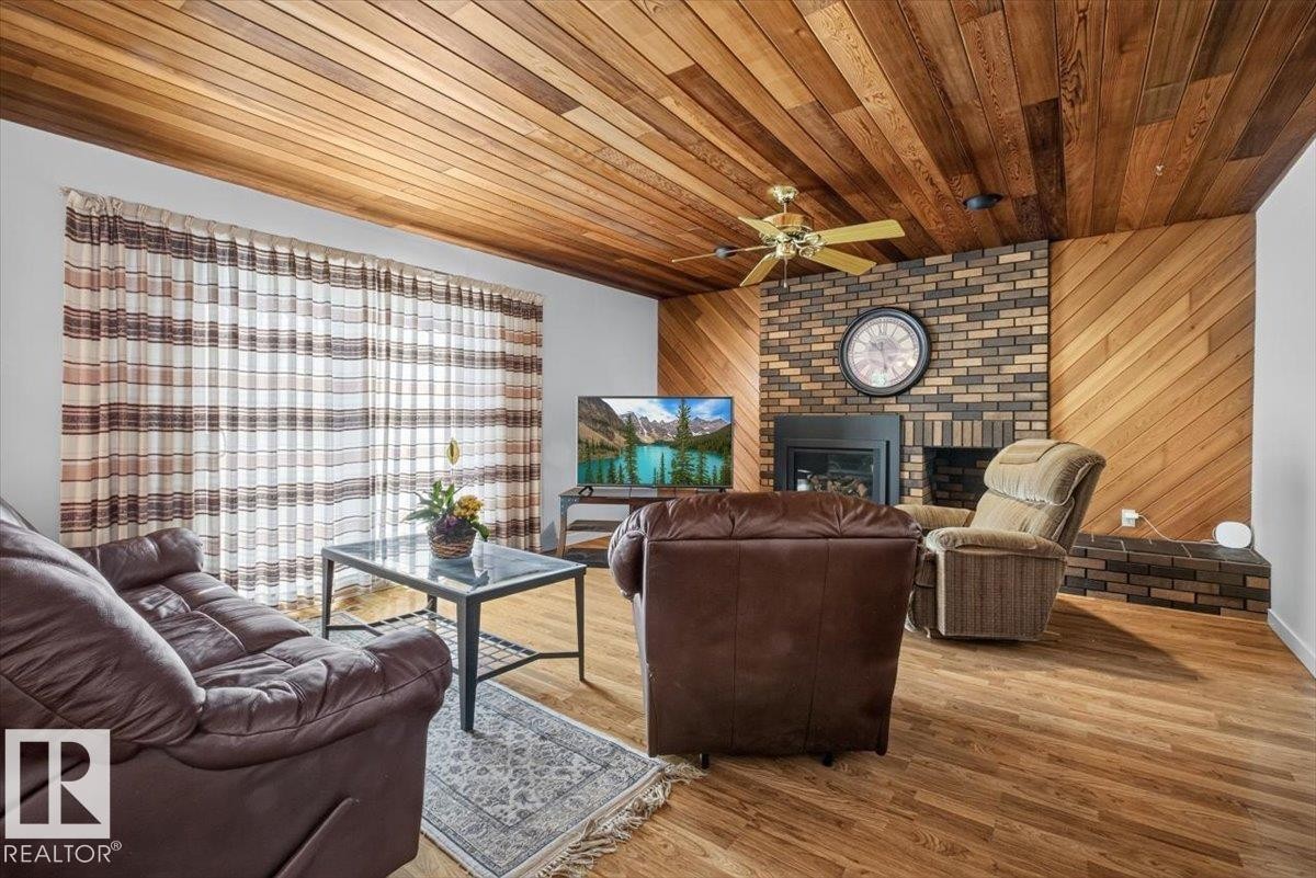 Living area featuring a brick fireplace surround with a black insert, wood-finish flooring, and a wood plank ceiling - 4027 74 Street Nw, Edmonton, AB - Indoor Photo Showing Living Room With Fireplace