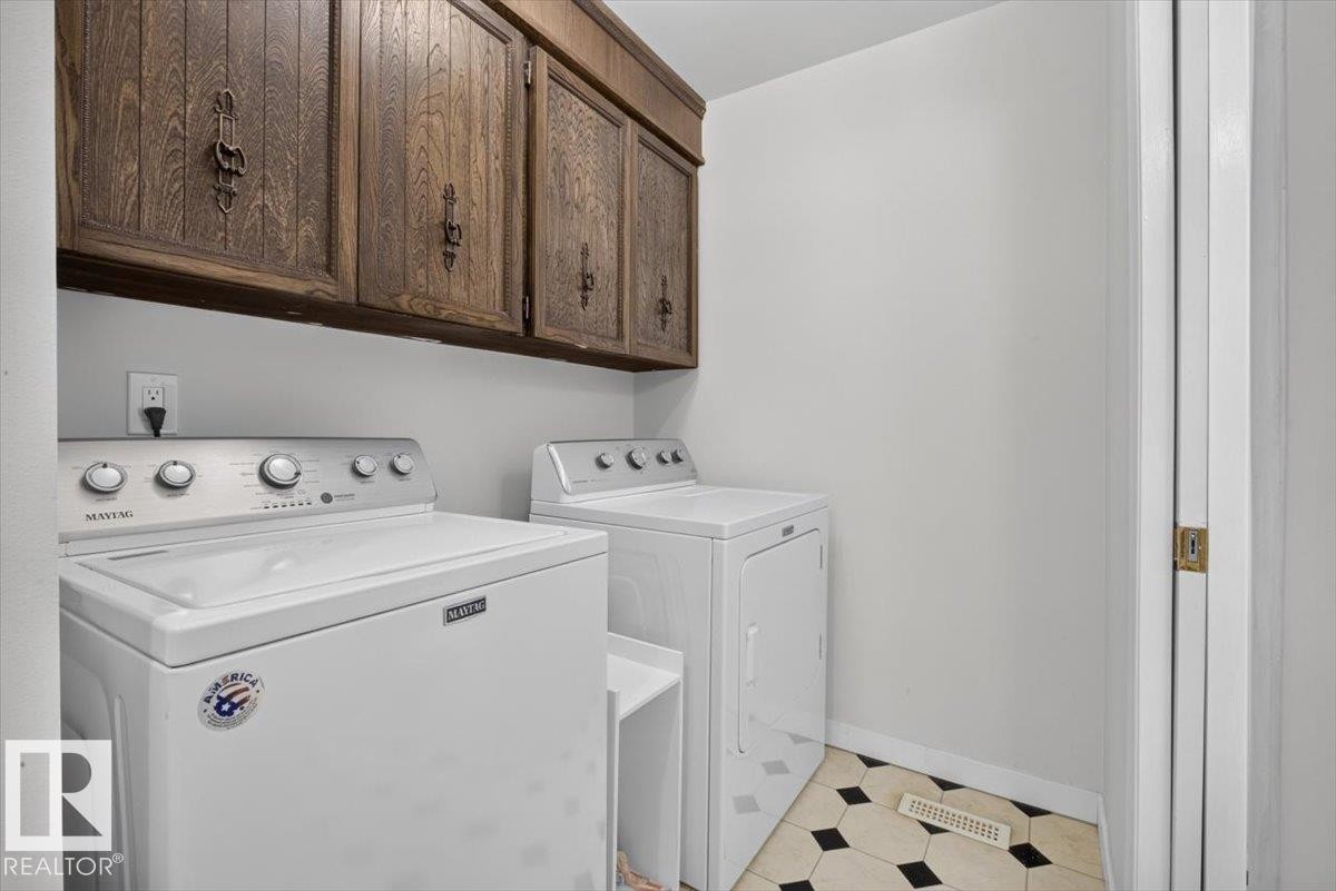 Laundry area featuring wood-finish cabinetry, white walls, and geometric black and white floor tiles - 4027 74 Street Nw, Edmonton, AB - Indoor Photo Showing Laundry Room