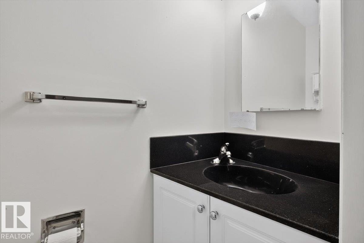 Bathroom vanity featuring a black countertop with an integrated black sink, polished chrome faucet, and white cabinetry with round chrome hardware - 4027 74 Street Nw, Edmonton, AB - Indoor