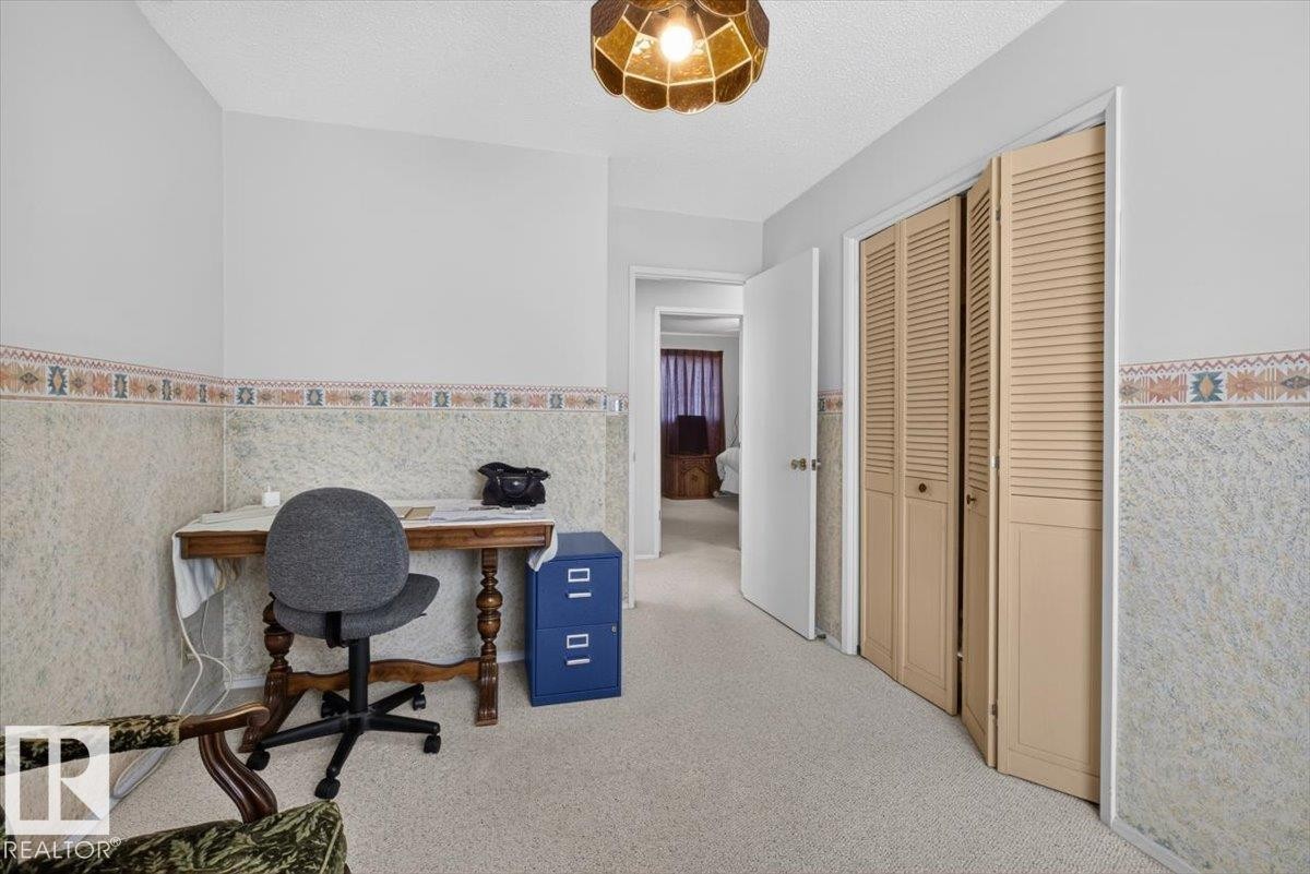 Carpeted room featuring a ceiling-mounted light fixture, louvered bi-fold closet doors, a white door, and textured wall paneling with a decorative border - 4027 74 Street Nw, Edmonton, AB - Indoor