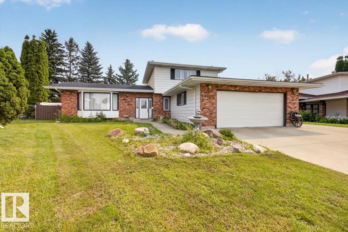 Split-level residence featuring a brick and white siding facade, an attached garage with a concrete driveway, and a front lawn with mature trees and established landscaping - 4027 74 Street Nw, Edmonton, AB - Outdoor With Facade