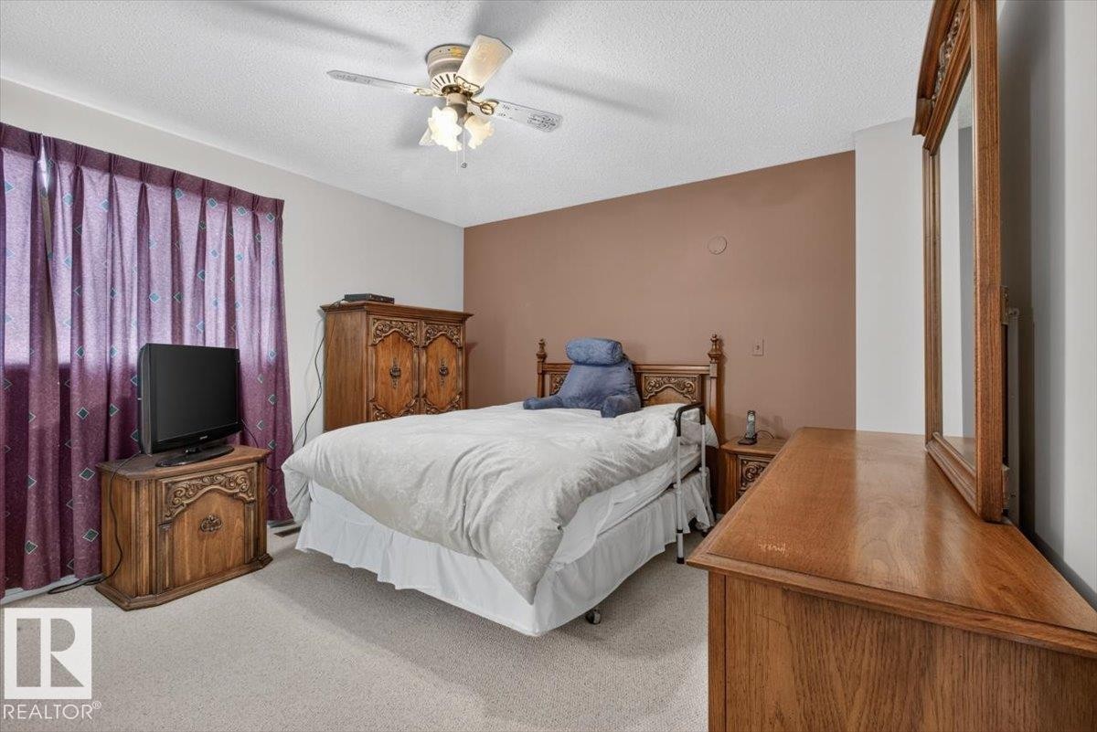 Carpeted interior space featuring a ceiling fan with integrated lighting, a contrasting accent wall, and a window with drapery - 4027 74 Street Nw, Edmonton, AB - Indoor Photo Showing Bedroom