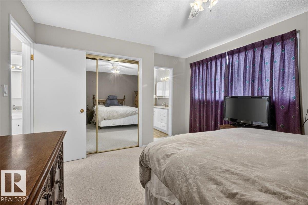 Carpeted interior space featuring a window with patterned drapes, a ceiling fan with integrated lighting, and a mirrored closet door - 4027 74 Street Nw, Edmonton, AB - Indoor Photo Showing Bedroom