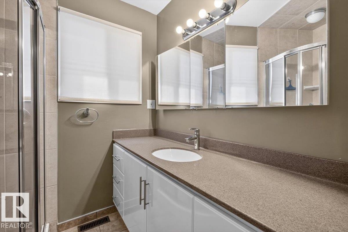 Bathroom featuring a spacious vanity with an integrated sink, ample storage cabinetry, and a wide mirror with overhead lighting - 4027 74 Street Nw, Edmonton, AB - Indoor Photo Showing Bathroom