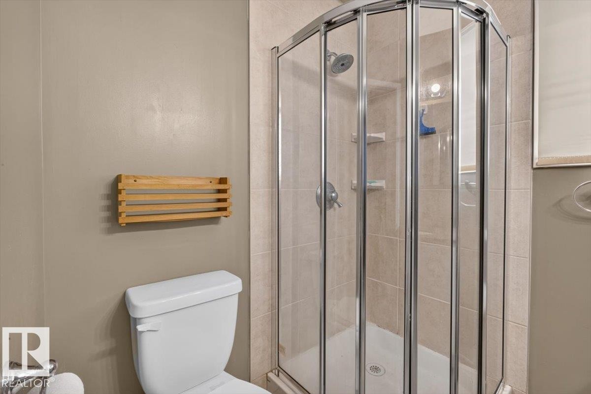 Glass-enclosed corner shower with a chrome shower head and light-toned tile surround - 4027 74 Street Nw, Edmonton, AB - Indoor Photo Showing Bathroom