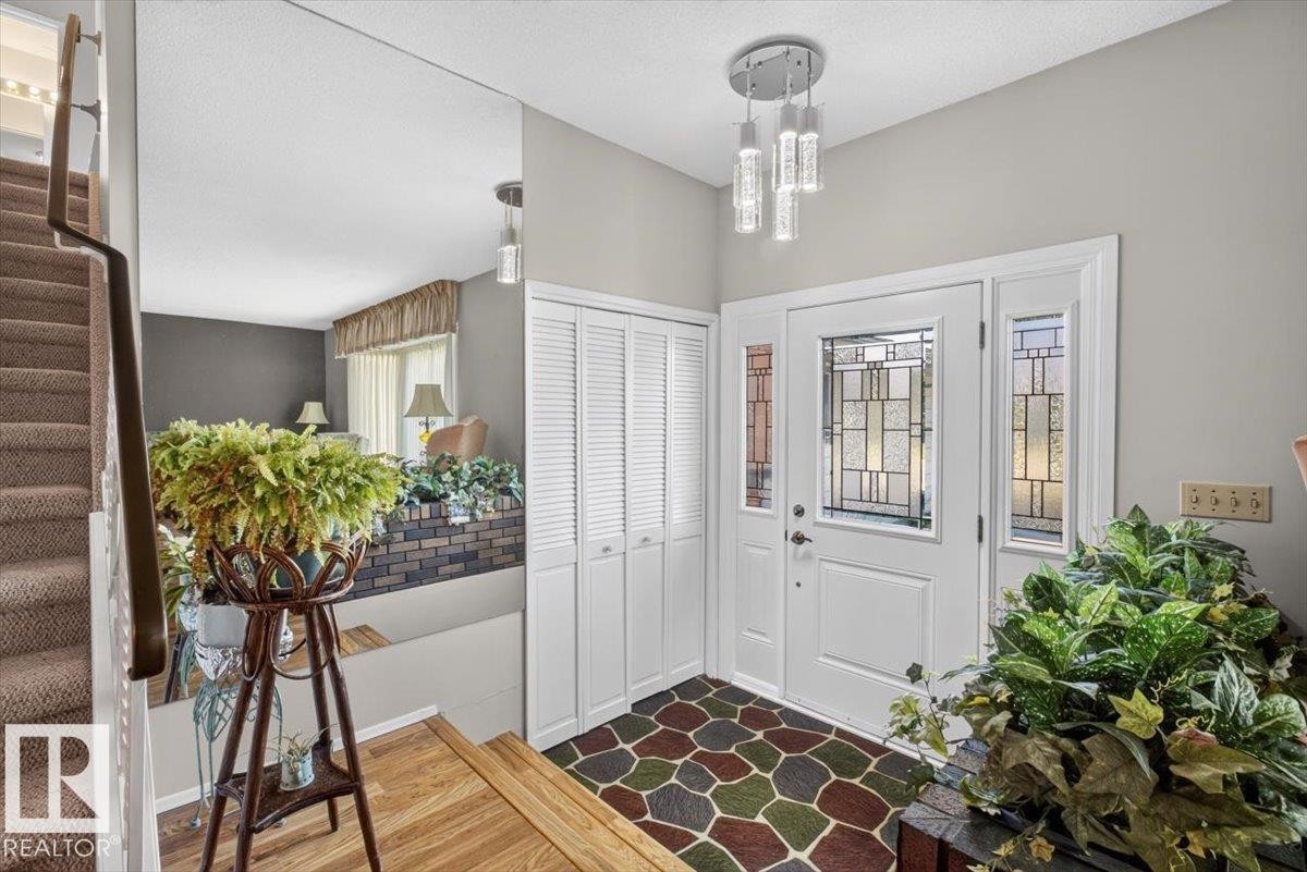 Entryway featuring a decorative glass front door with coordinating sidelights, a contemporary multi-bulb ceiling fixture, a mosaic-patterned floor, and bi-fold closet doors - 4027 74 Street Nw, Edmonton, AB - Indoor Photo Showing Other Room