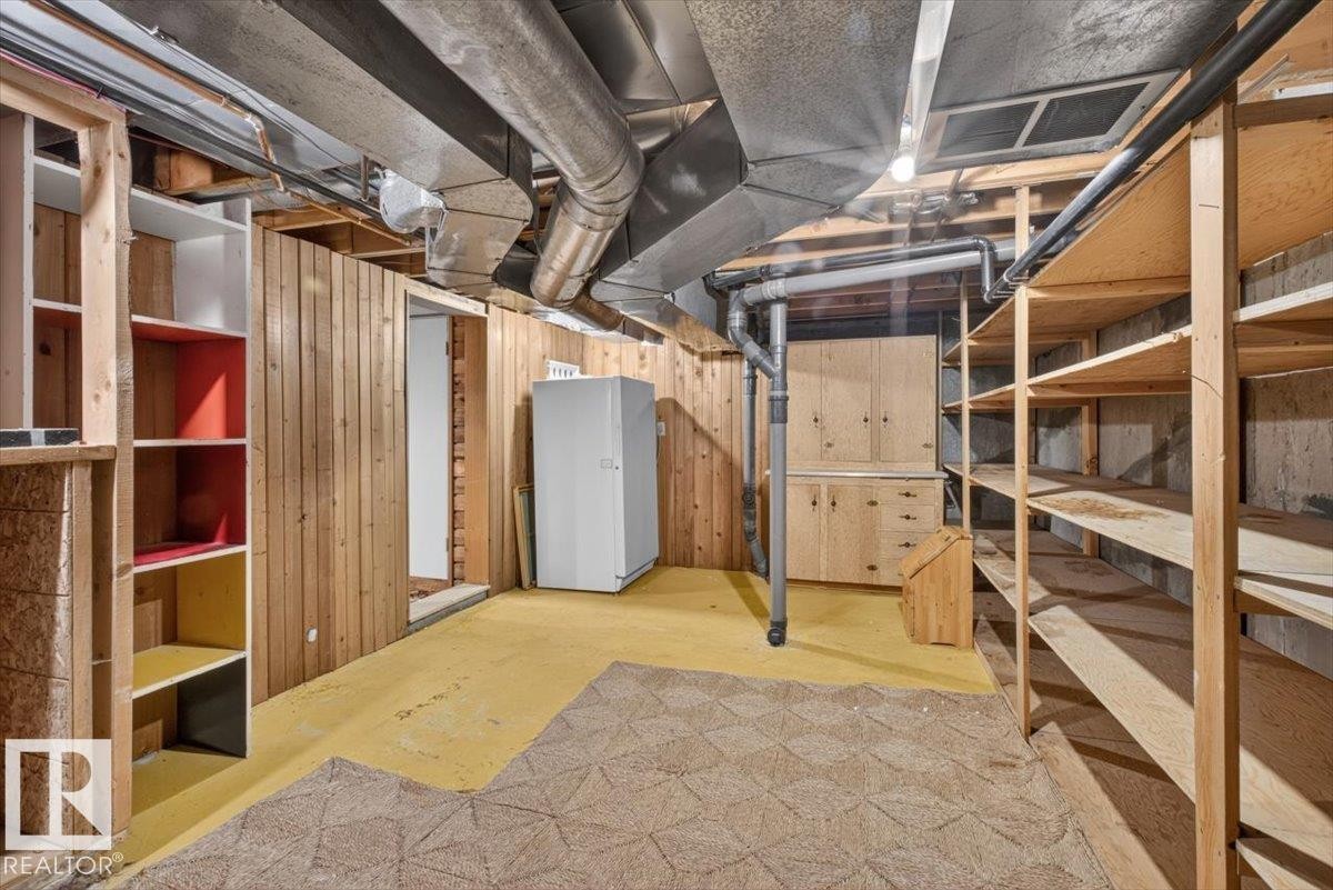 Lower level utility room featuring extensive built-in shelving, wood-paneled walls, exposed ductwork, and a built-in wooden cabinet - 4027 74 Street Nw, Edmonton, AB - Indoor Photo Showing Basement