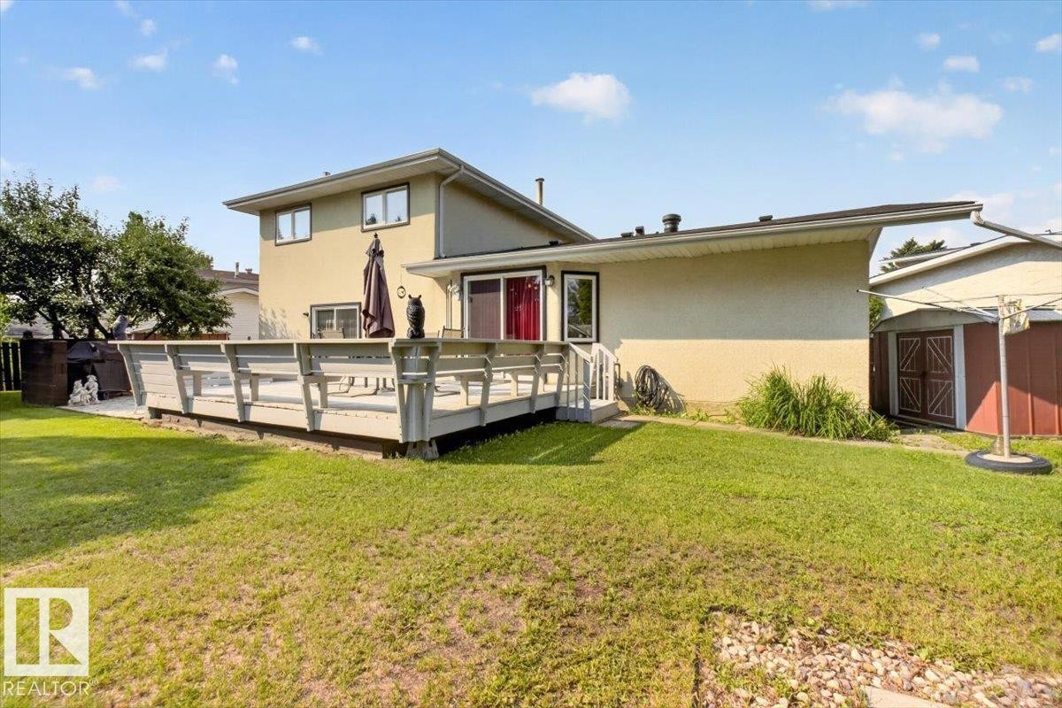 Expansive rear yard featuring a large elevated deck, stucco exterior, multiple windows, and a storage shed - 4027 74 Street Nw, Edmonton, AB - Outdoor