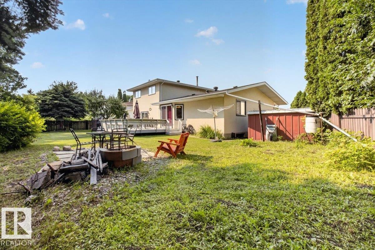 Expansive backyard featuring a built-in fire pit, a wooden deck, and mature perimeter trees - 4027 74 Street Nw, Edmonton, AB - Outdoor With Deck Patio Veranda