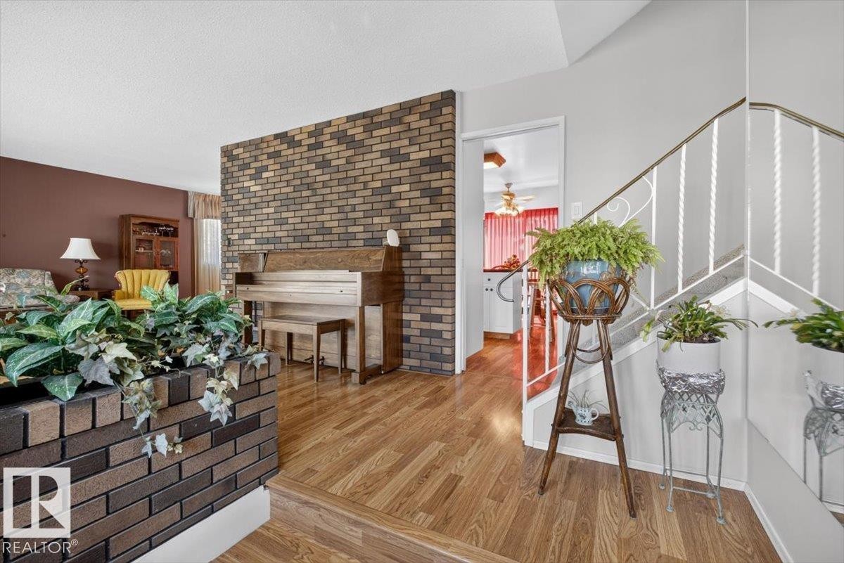 Interior entryway featuring wood-finish flooring, a brick accent wall, and a white metal staircase railing - 4027 74 Street Nw, Edmonton, AB - Indoor Photo Showing Other Room