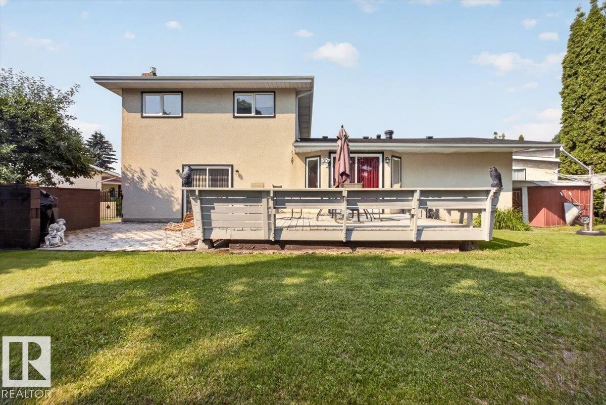 Expansive backyard featuring a large green lawn, multi-level wood deck, stone patio, and a mature evergreen tree - 4027 74 Street Nw, Edmonton, AB - Outdoor