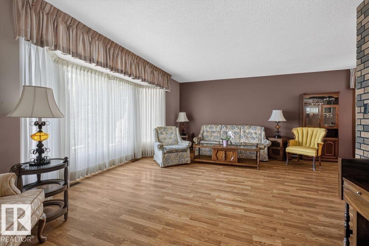 Spacious living area featuring expansive windows with custom valances, wood-finish flooring, a neutral ceiling, and a brick accent wall - 4027 74 Street Nw, Edmonton, AB - Indoor Photo Showing Living Room