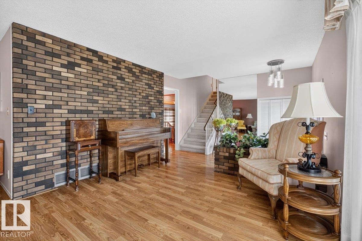 Interior space featuring wood-finish flooring, a prominent brick accent wall, and a carpeted staircase with a dark railing - 4027 74 Street Nw, Edmonton, AB - Indoor