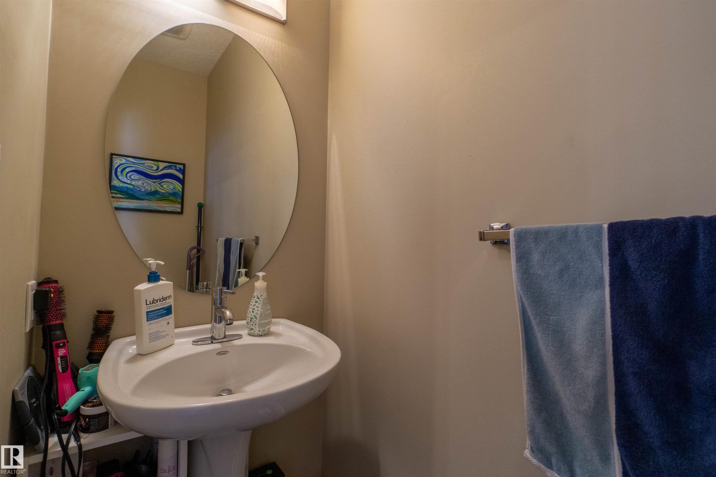 Pedestal sink with a polished chrome faucet, oval wall mirror, and wall-mounted light fixture - #75 8315 180 Av Nw, Edmonton, AB