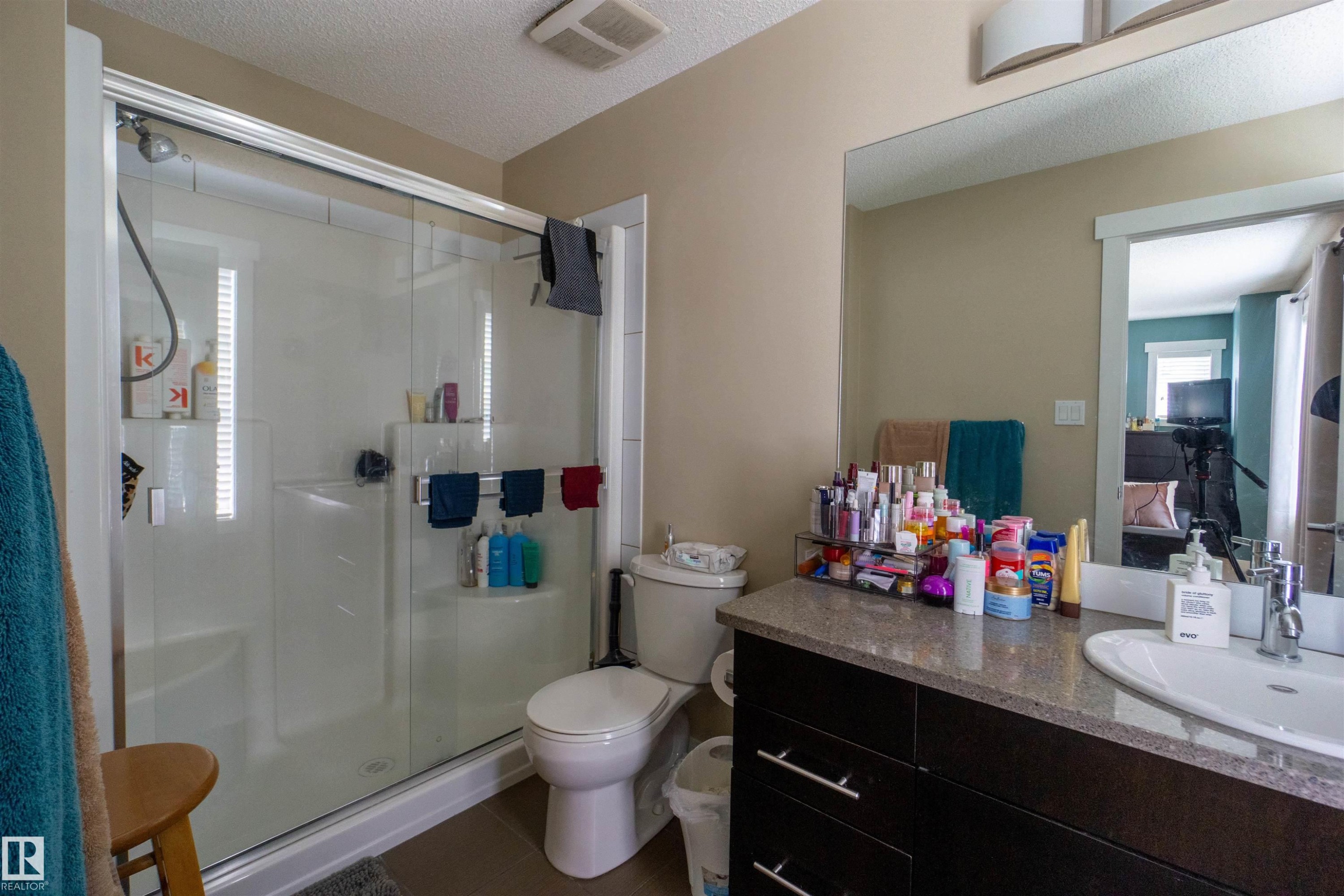 Glass-enclosed shower with integrated shelving, single vanity with a white basin sink, dark wood-finish cabinetry, and a framed mirror - #75 8315 180 Av Nw, Edmonton, AB