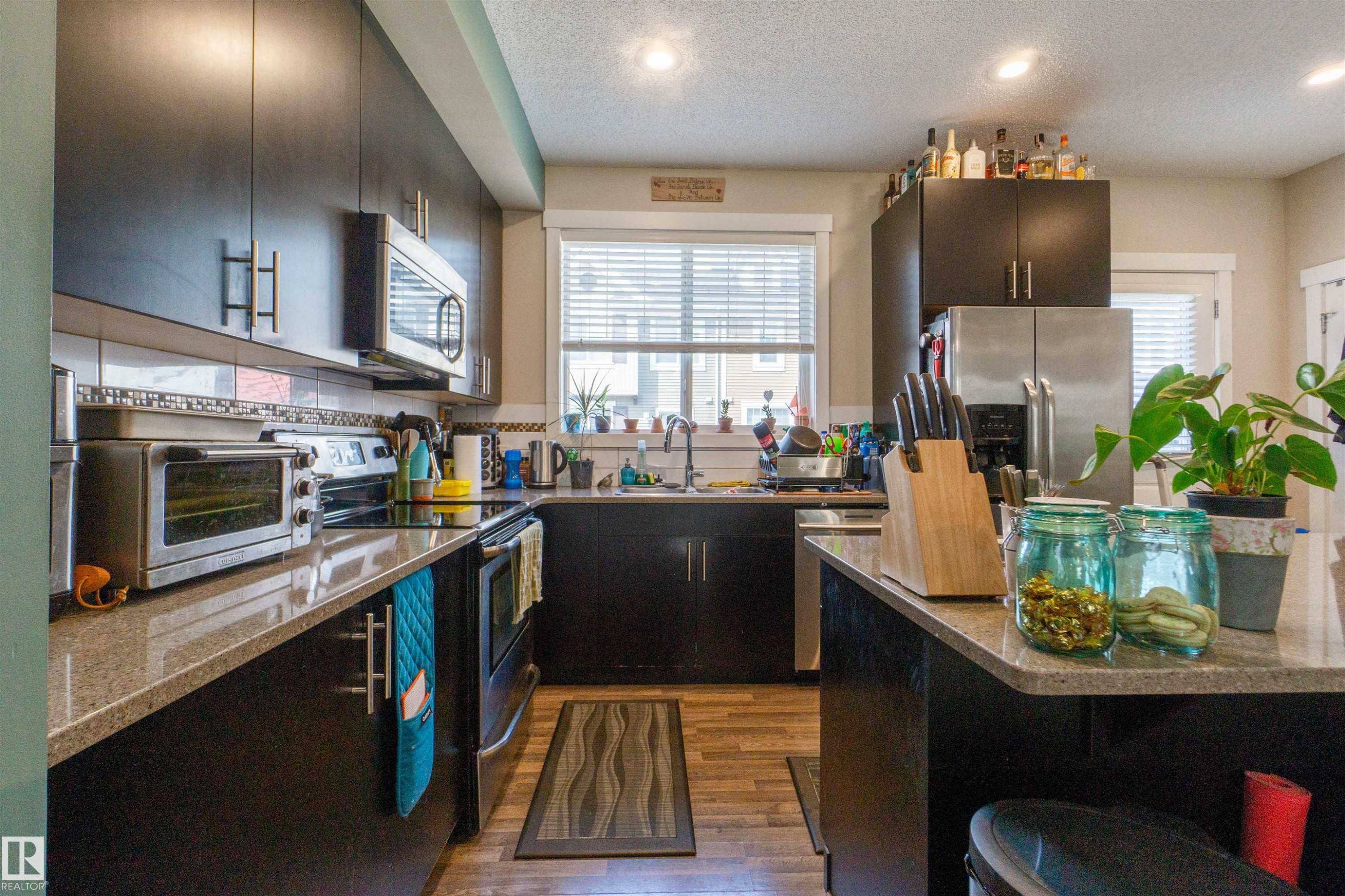 Modern kitchen featuring dark wood-finish cabinetry, stainless steel appliances, a built-in microwave, and wood-finish flooring - #75 8315 180 Av Nw, Edmonton, AB
