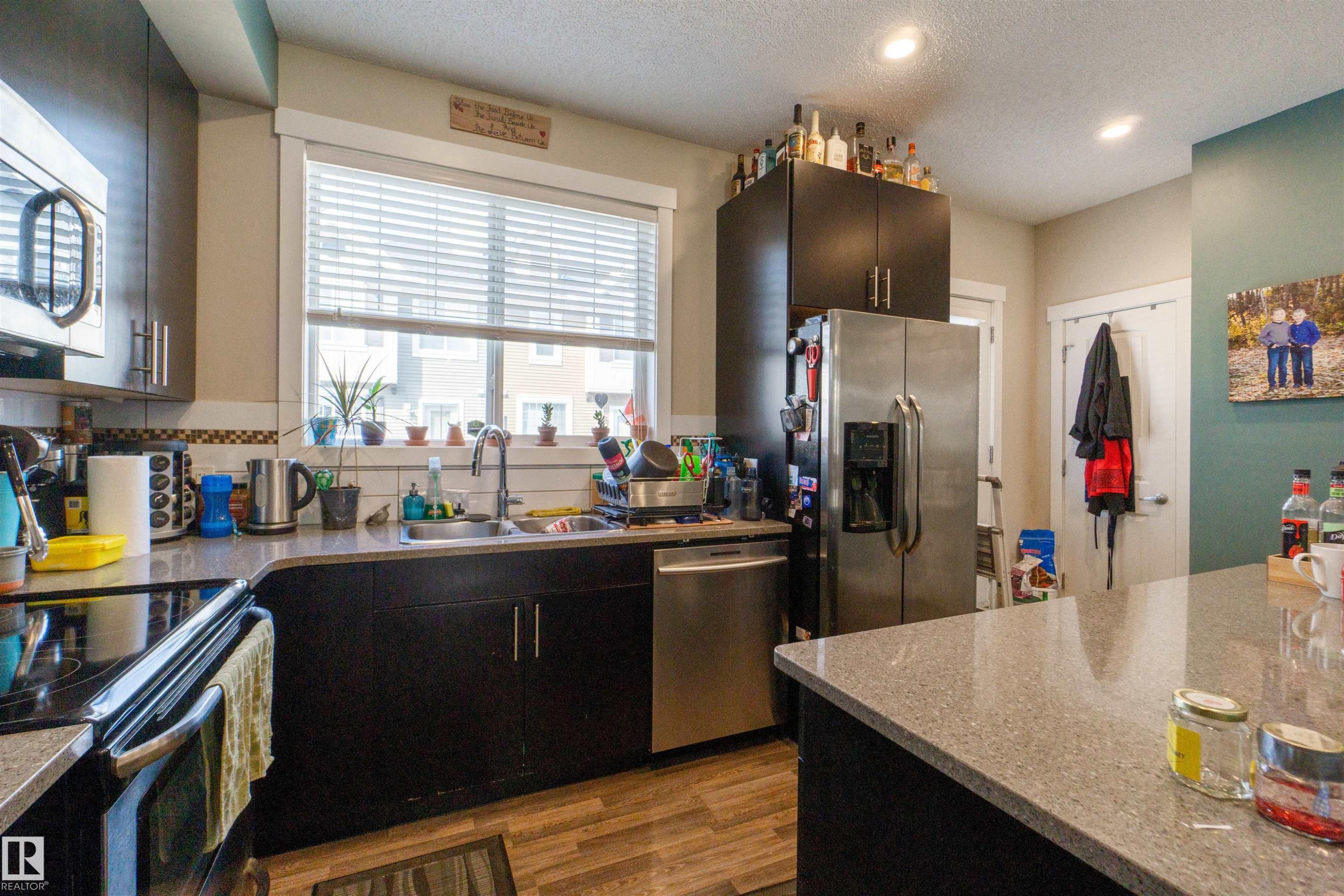 Kitchen with dark wood-finish cabinetry, stainless steel appliances, speckled stone countertops, and wood-finish flooring - #75 8315 180 Av Nw, Edmonton, AB