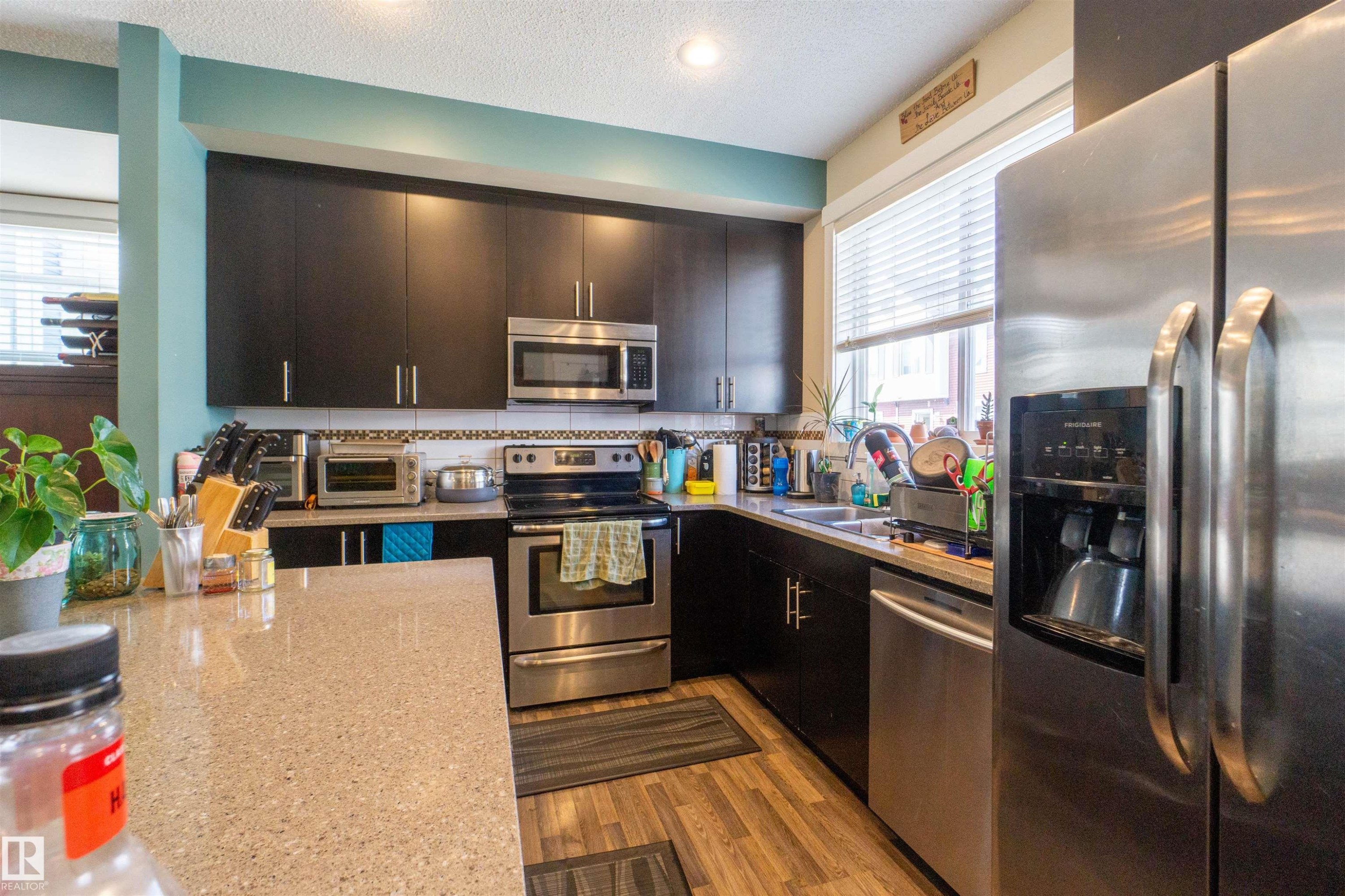 Kitchen featuring dark cabinetry, light-colored countertops, stainless steel appliances, and wood-finish flooring - #75 8315 180 Av Nw, Edmonton, AB