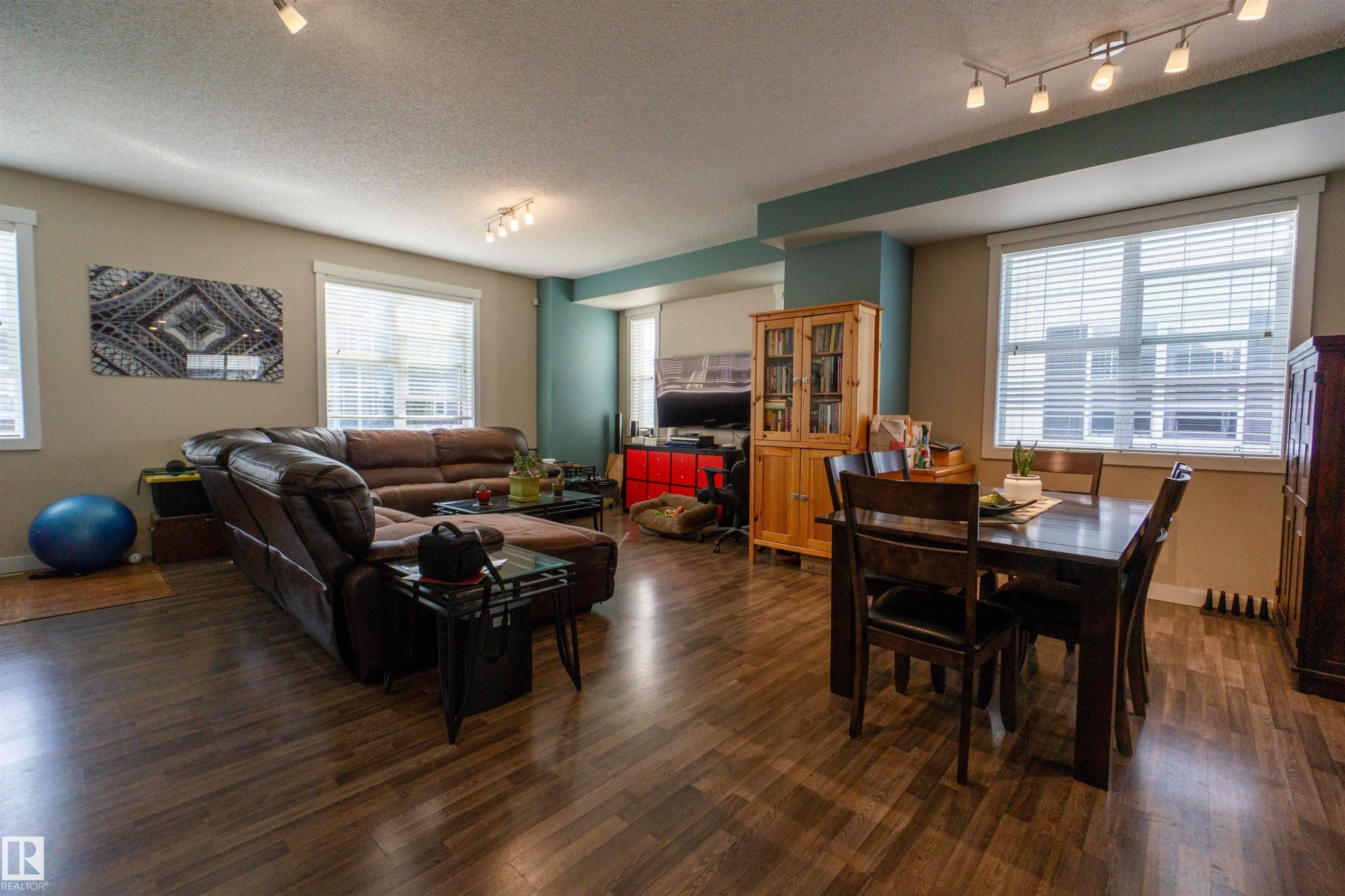 Wood-finish flooring throughout, track lighting, multiple windows, and a built-in wood cabinet - #75 8315 180 Av Nw, Edmonton, AB